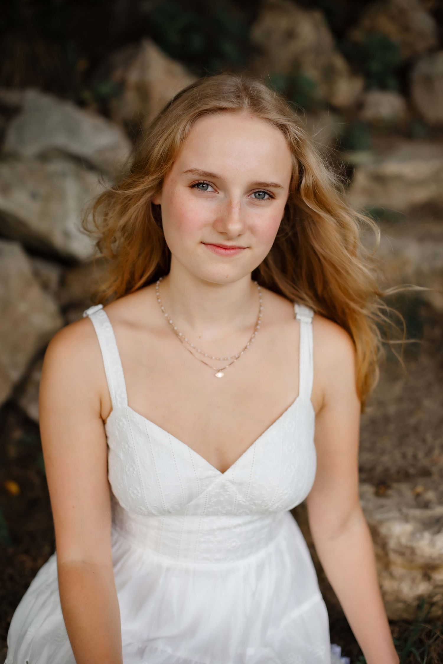 Portrait in white dress with flowing hair against rocky natural backdrop.