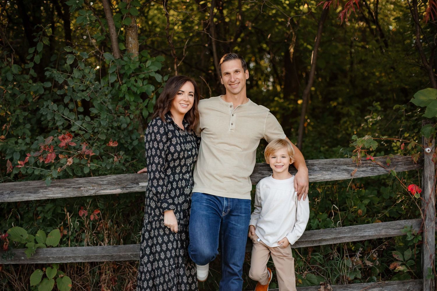 A family poses together against a rustic wooden fence at sunset in a garden setting.