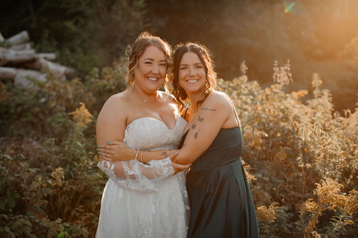 Sunset portrait of bride in white dress with bridesmaid in grey dress outdoors.