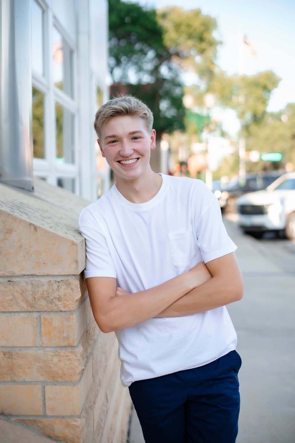 Relaxed outdoor portrait with crossed arms against brick wall with windows.