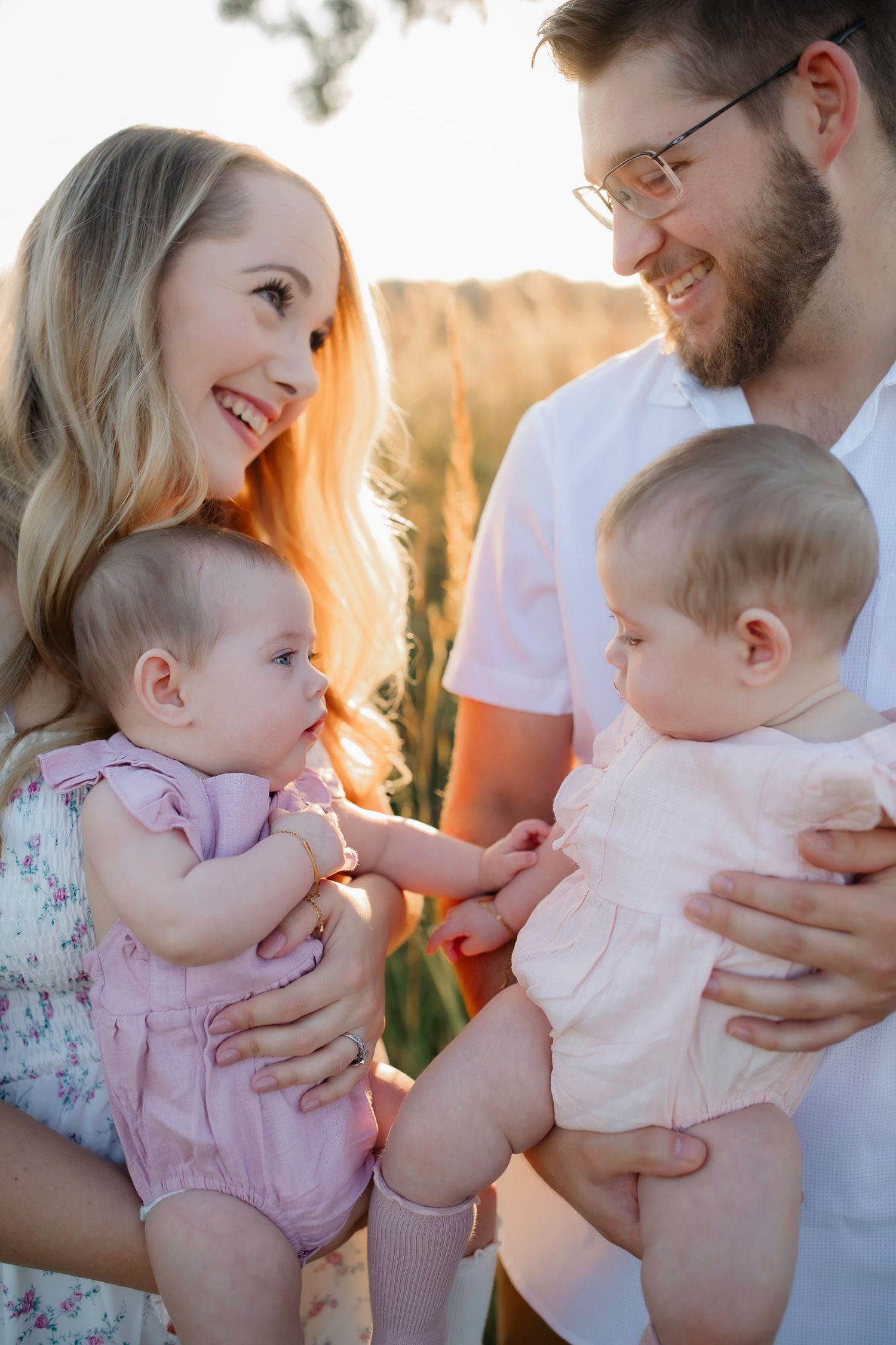 Candid family moment with twin babies in pink rompers during golden hour photoshoot.