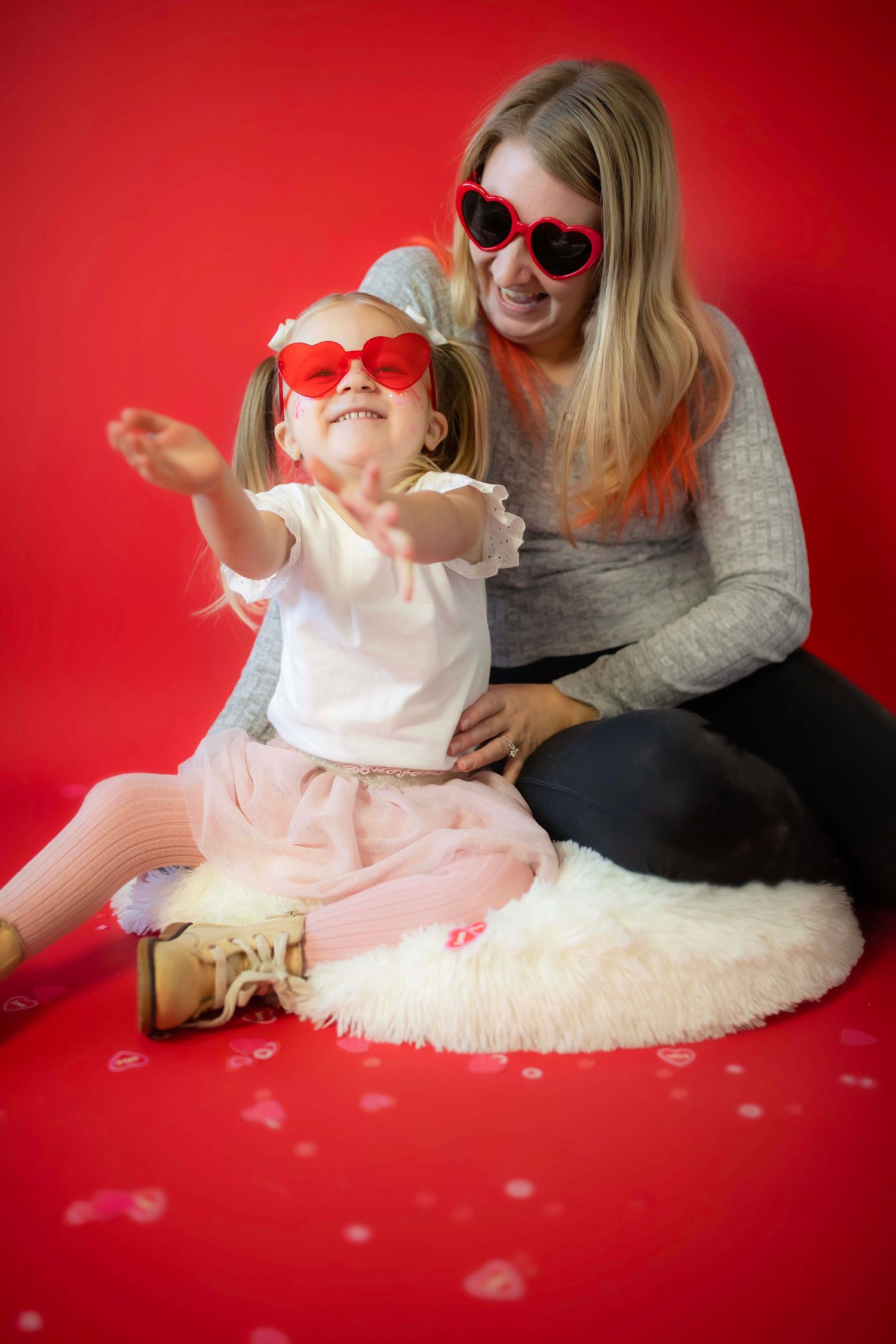 Playful Valentine's themed photo session with matching heart sunglasses on fuzzy white rug.