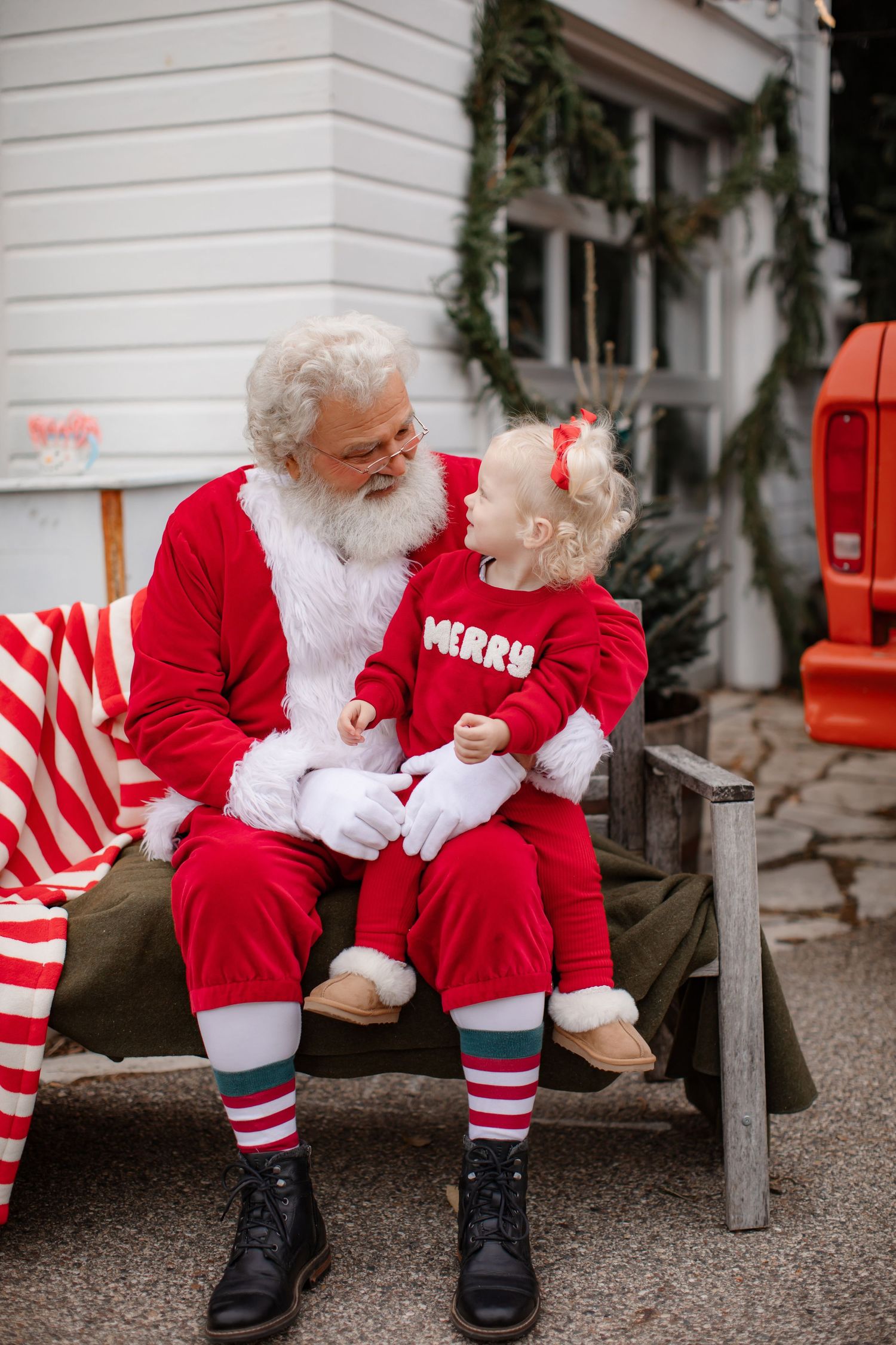 Santa Claus sharing a moment with toddler in red outfit on wooden bench.
