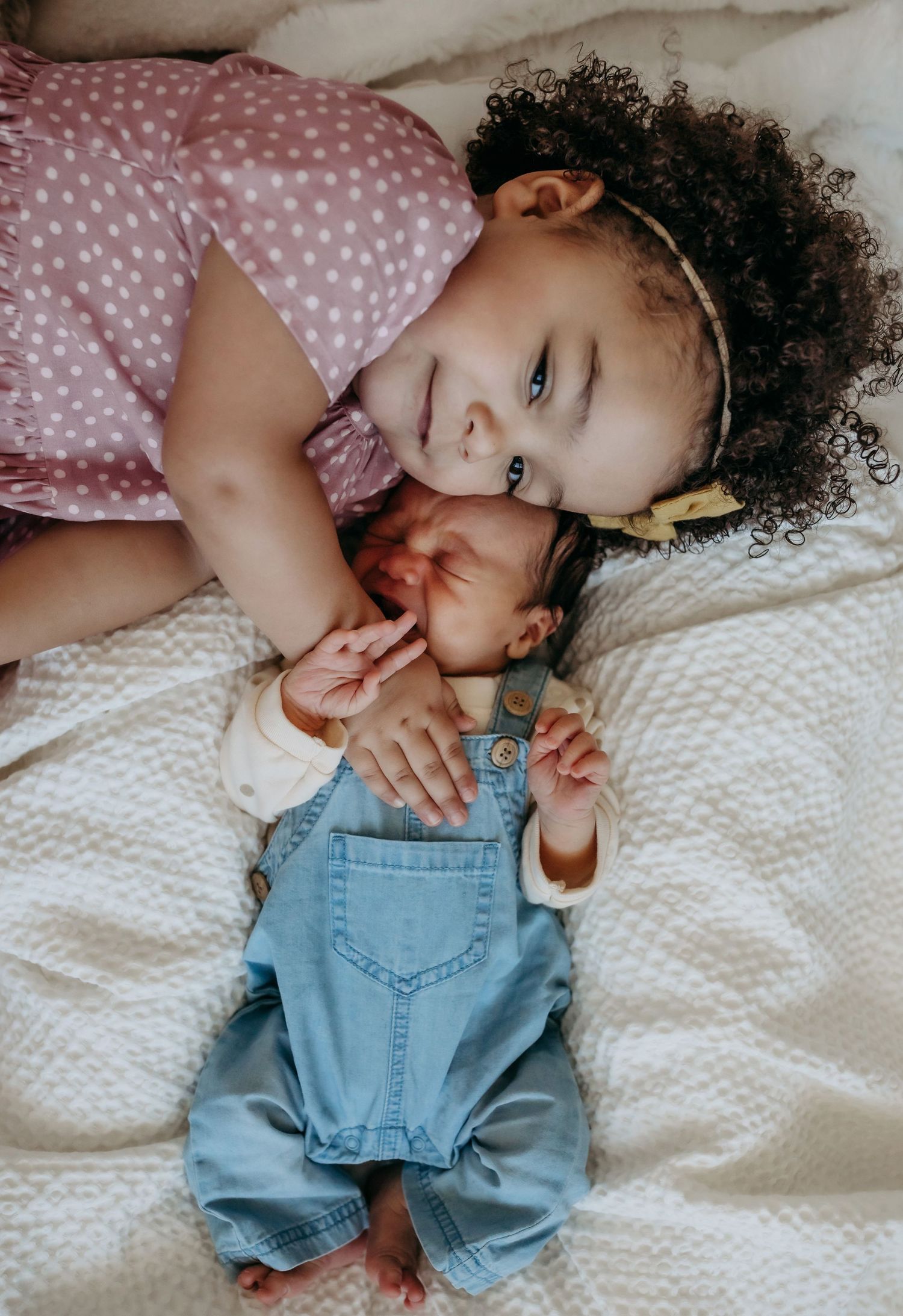 Two young children in casual outfits sharing a sweet moment on white bedding.