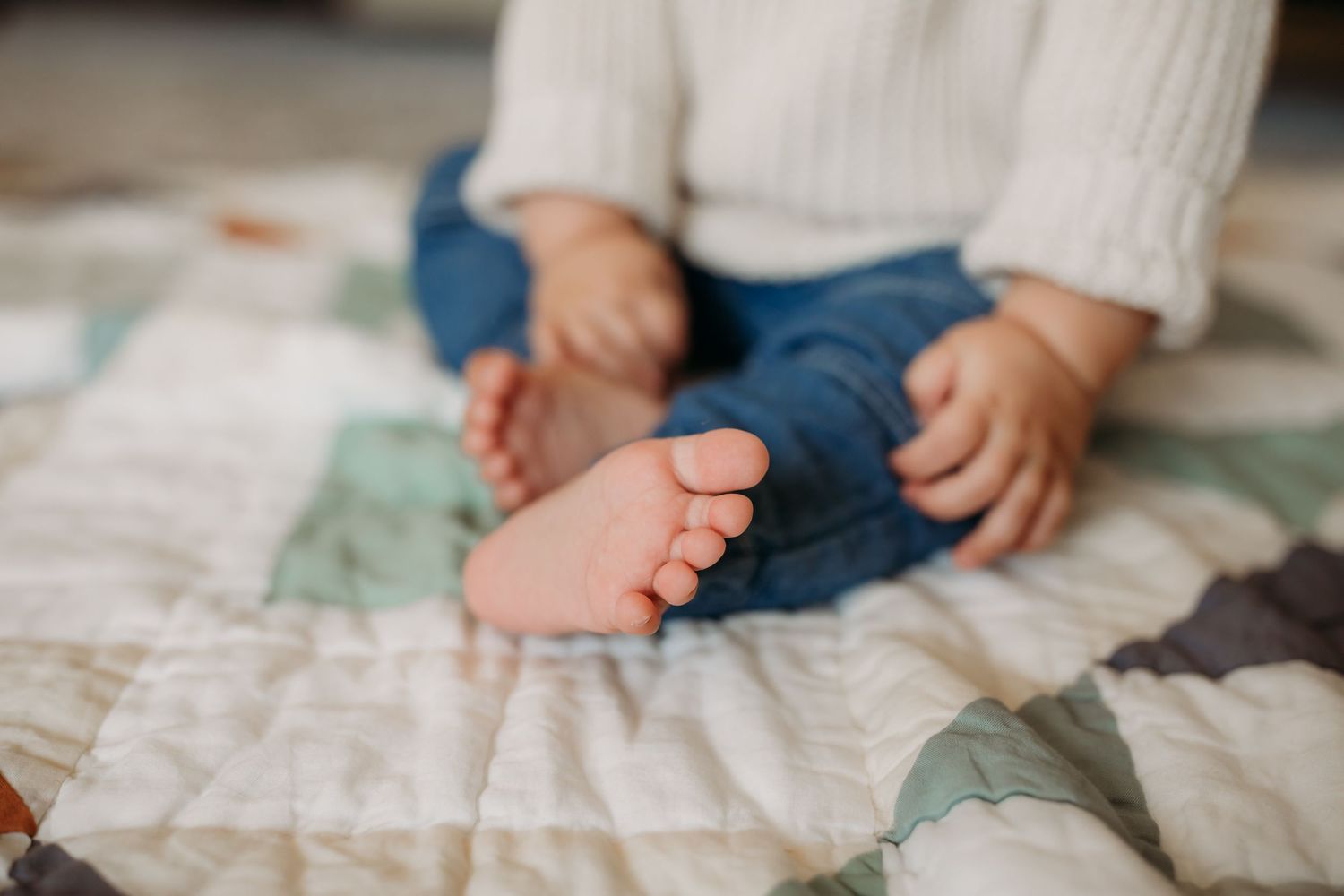 Close-up of small bare feet on a patterned quilt.