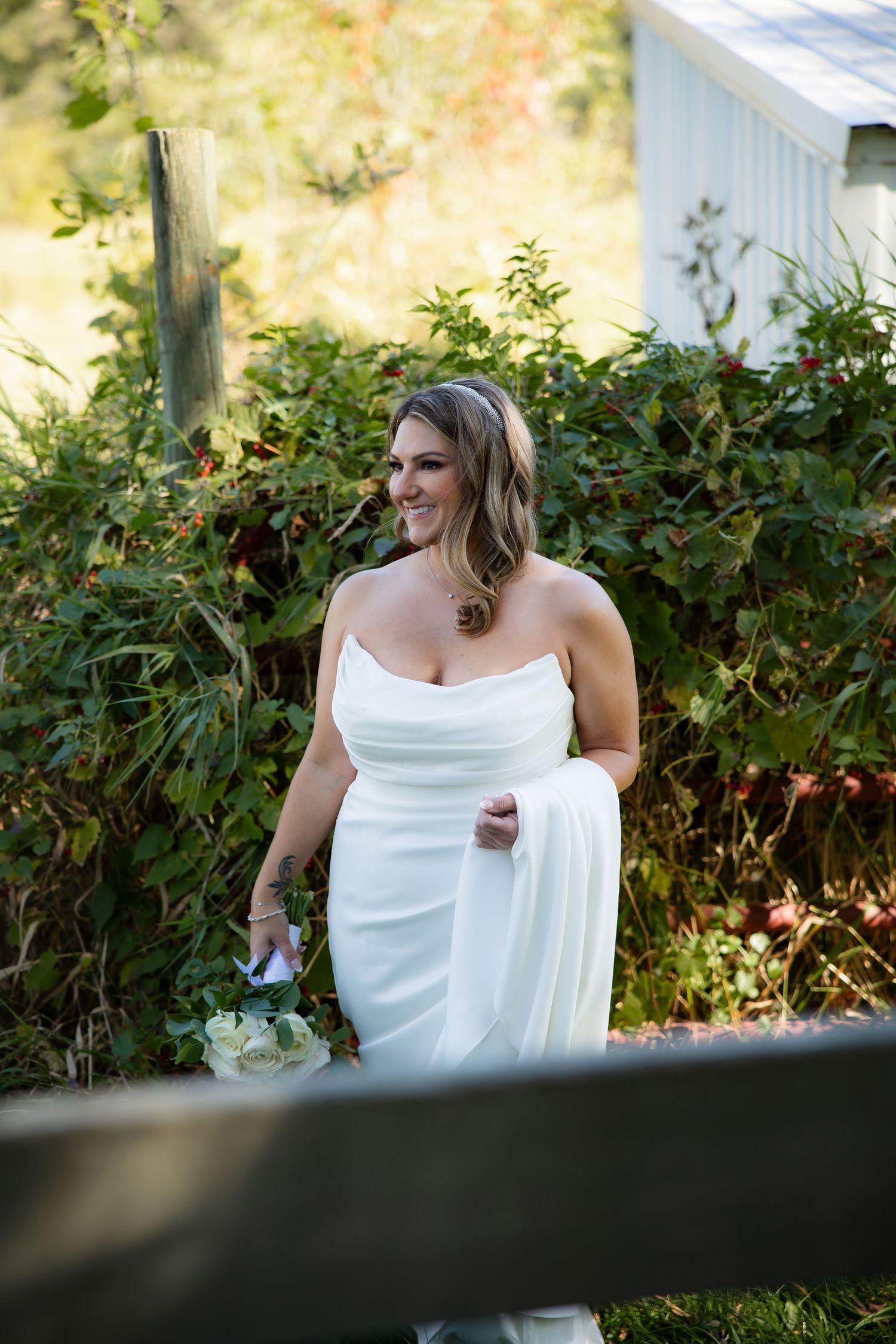 A bride in a white strapless gown poses outdoors against a garden backdrop.