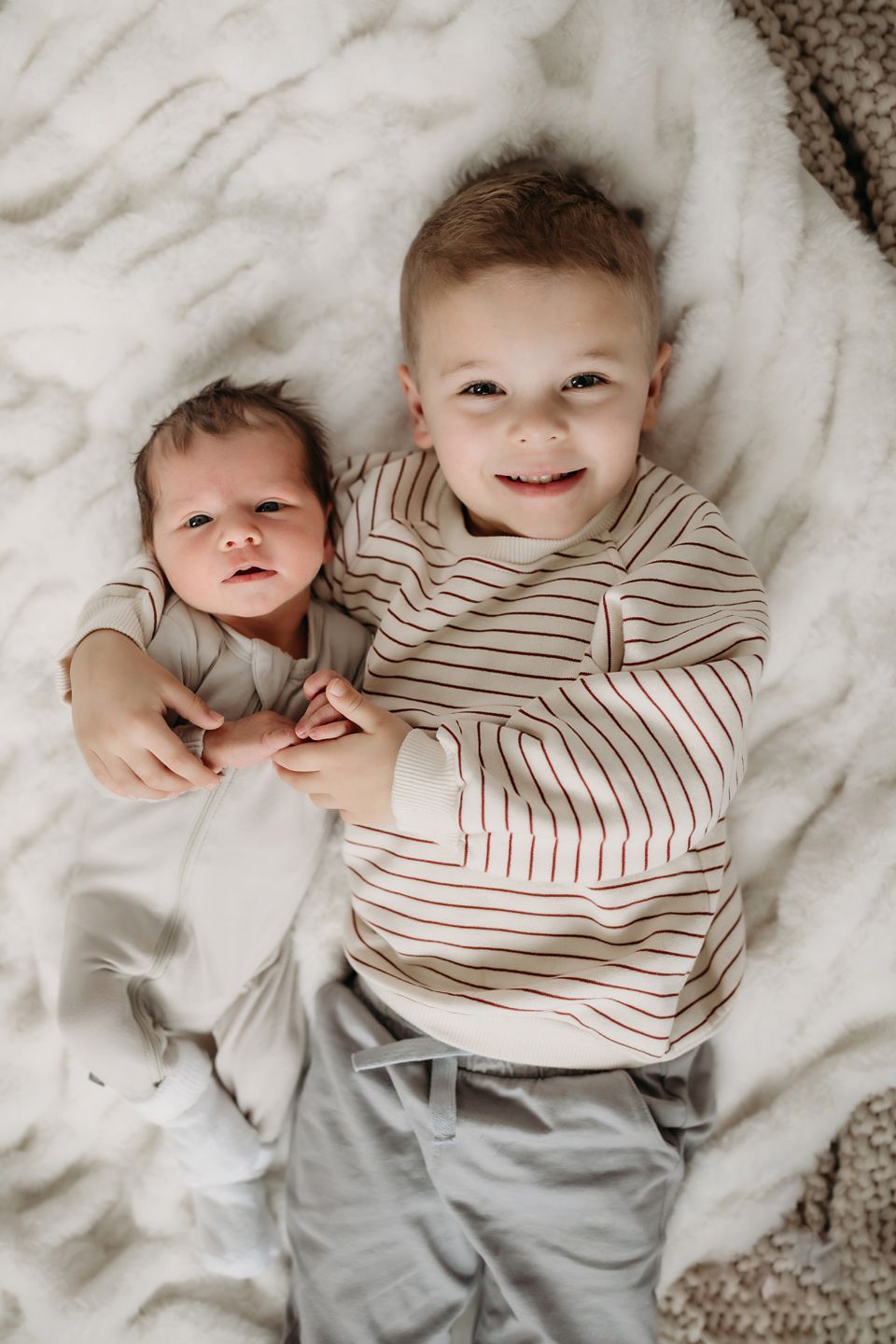 Two children in striped outfits lying on white blanket.