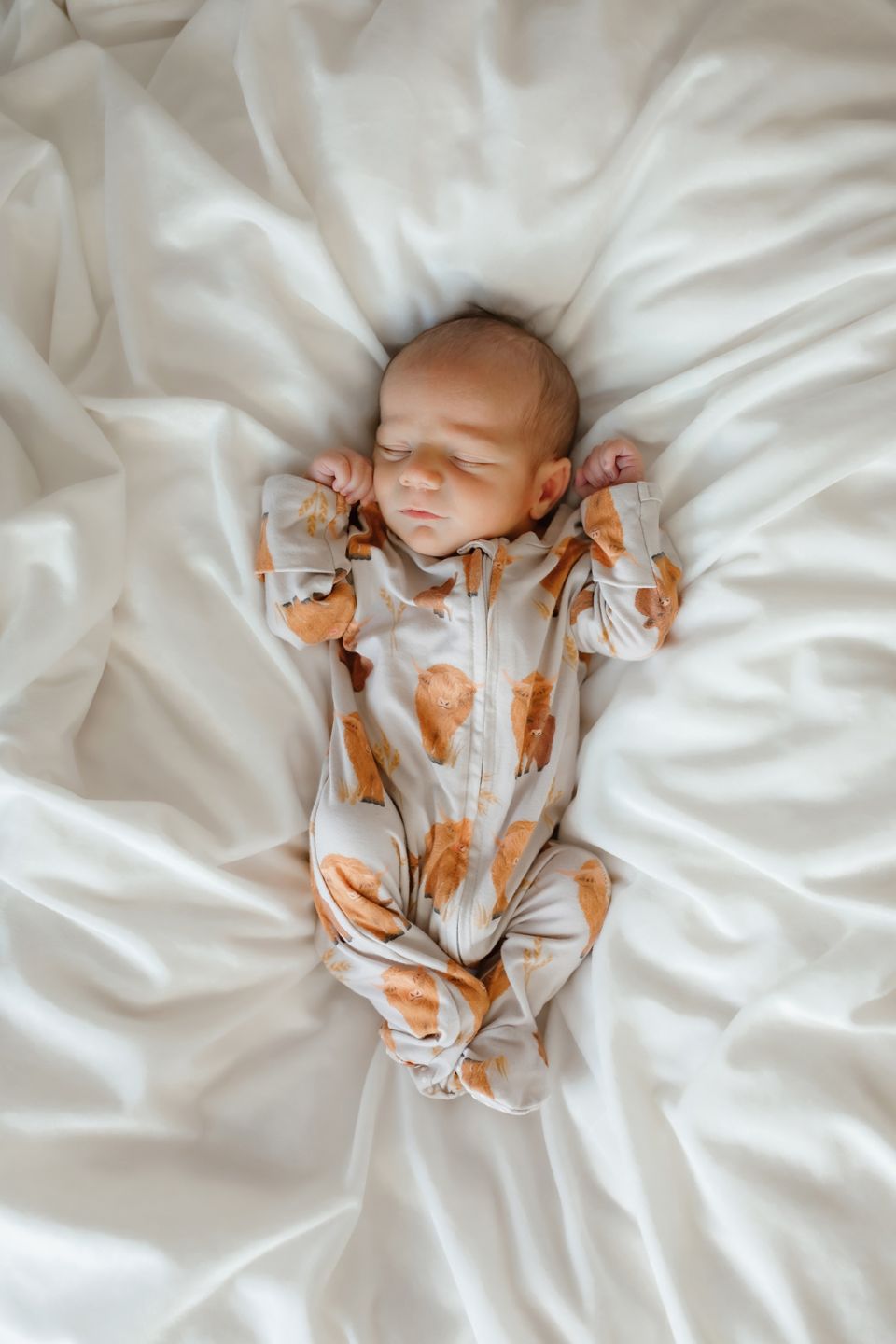 Peaceful newborn sleeps in orange patterned outfit on white sheets.