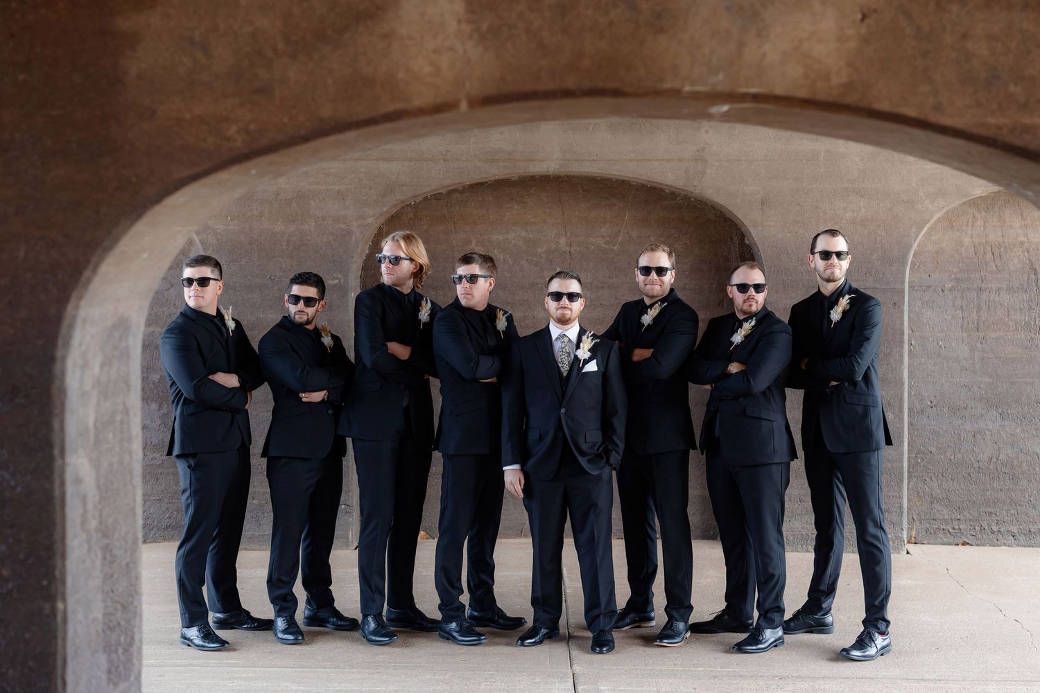 Wedding party strikes cool pose wearing sunglasses under concrete arch.