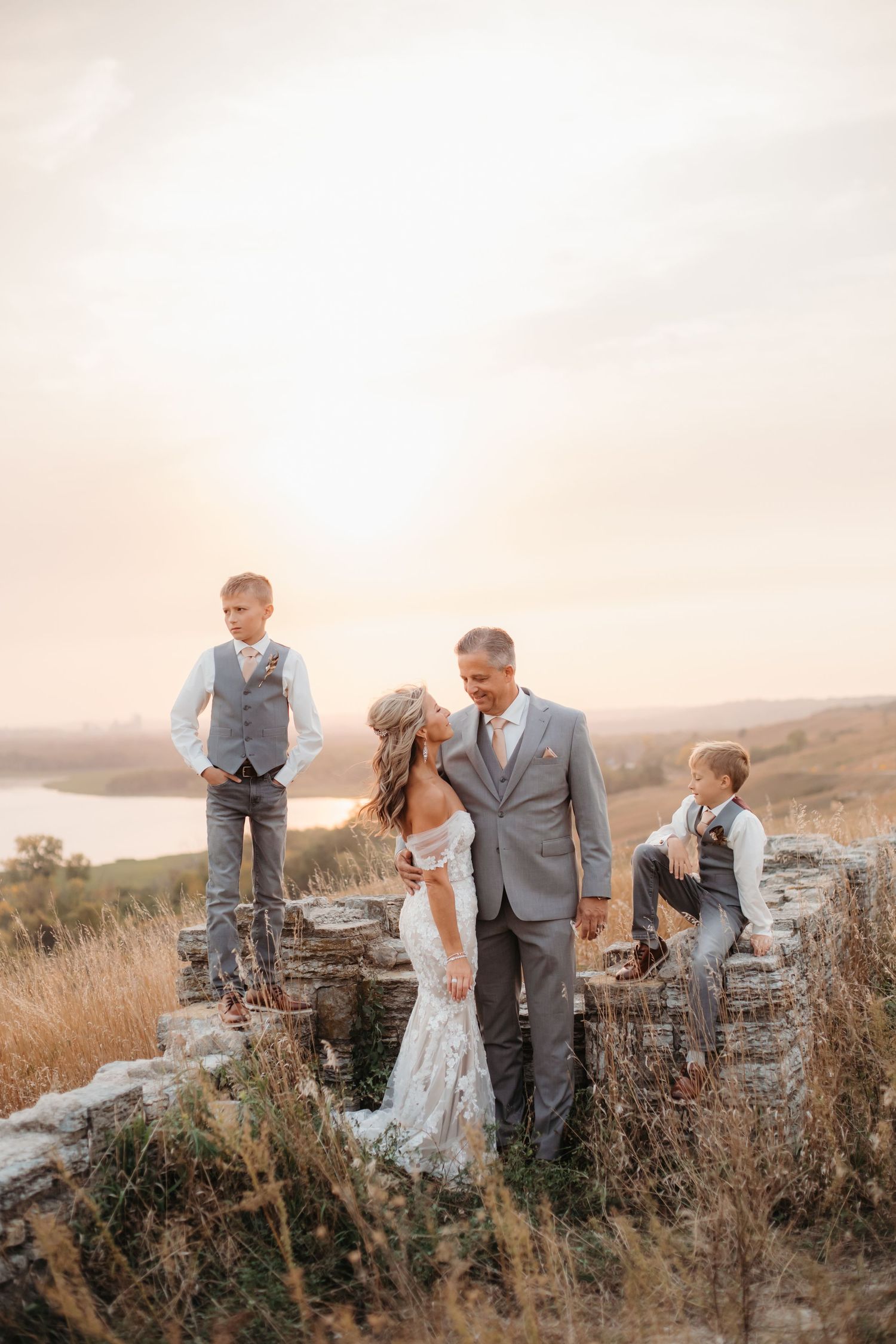 Family stands on stone wall during golden hour photoshoot with rolling hills in background.