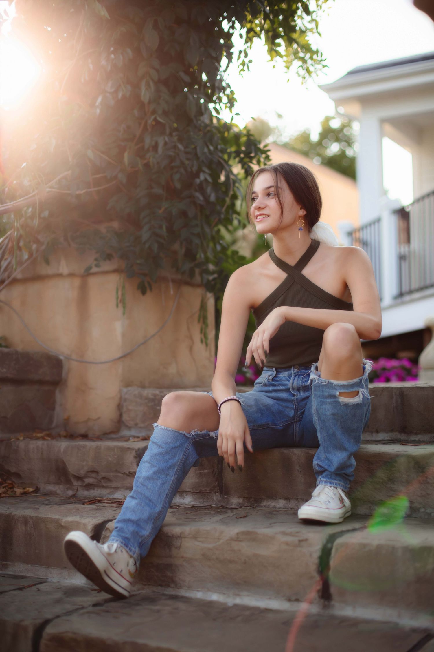 Person in halter top and jeans sitting on stone steps in warm sunlight.