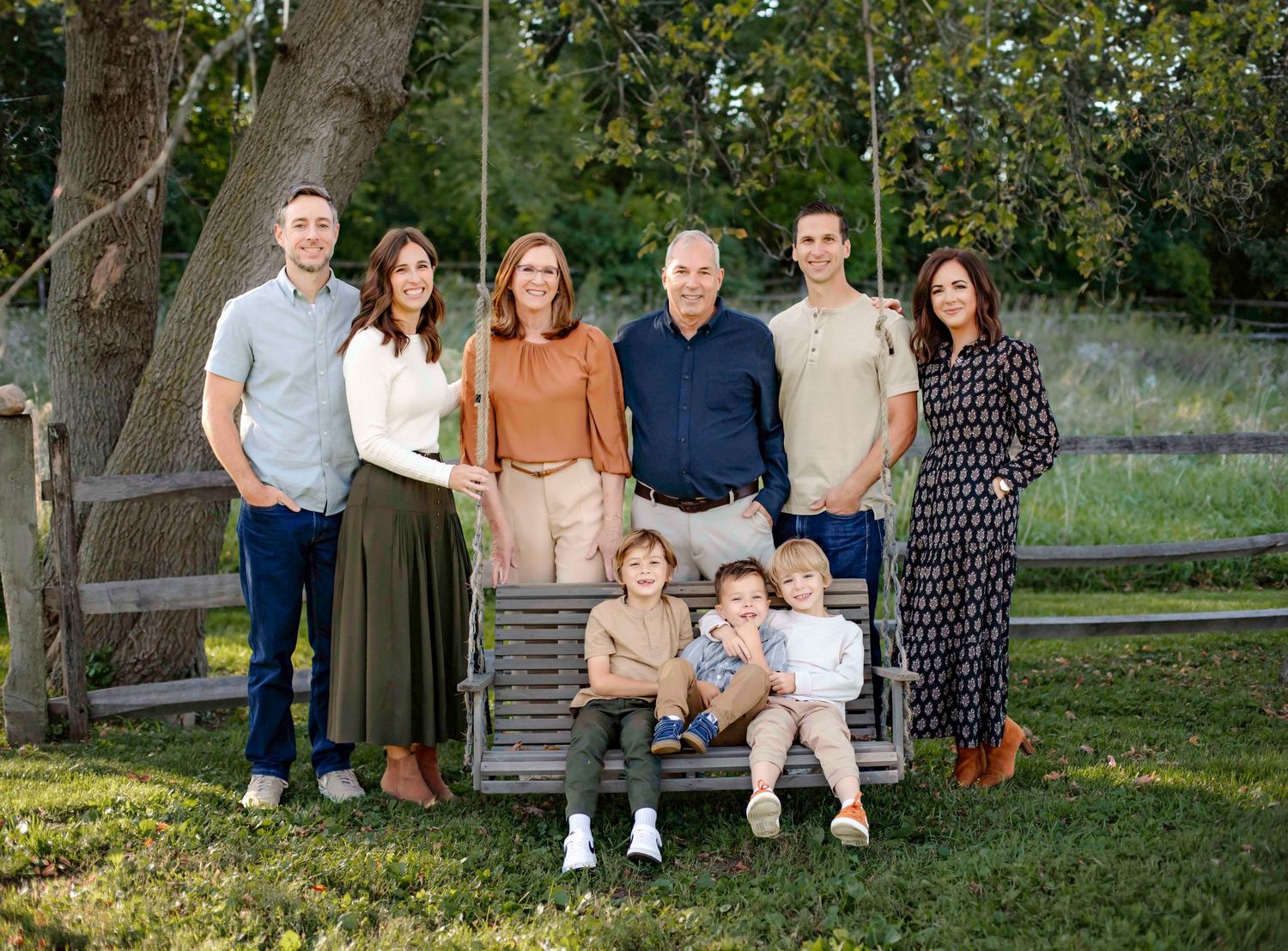 Extended family group poses together on wooden bench in garden setting at sunset.