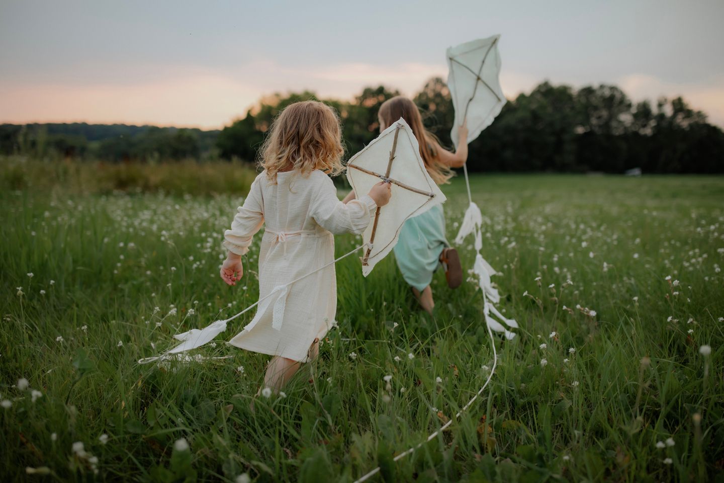 Children running with handmade kites through a field of wildflowers at dusk.