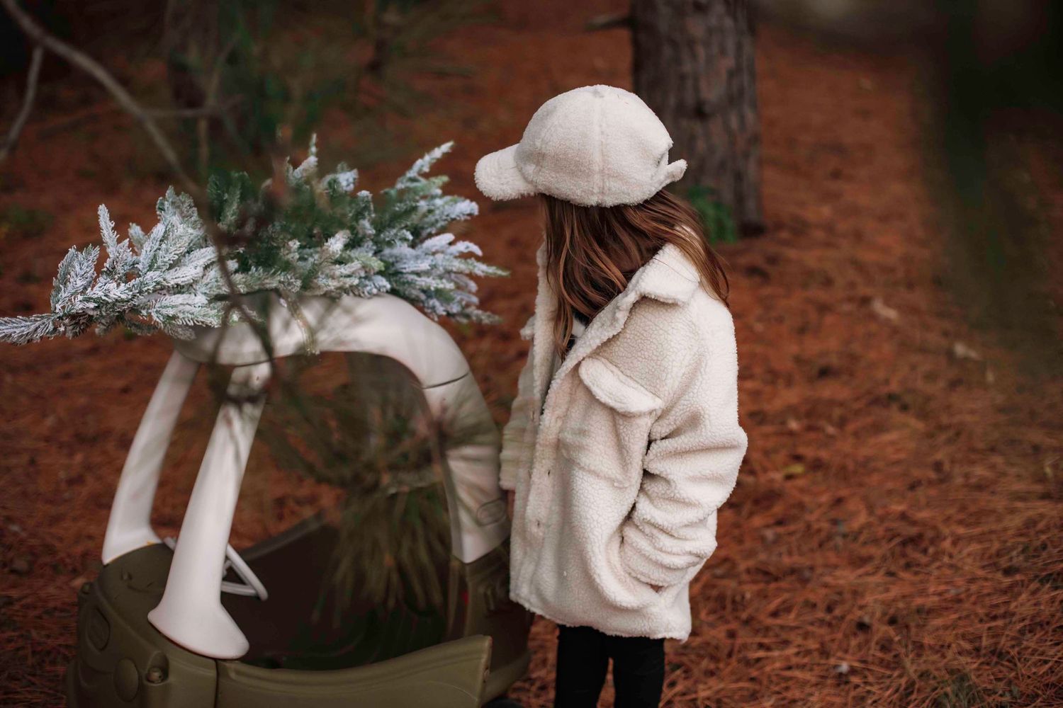 A cozy winter outfit paired with a small decorated wagon on a dirt path.
