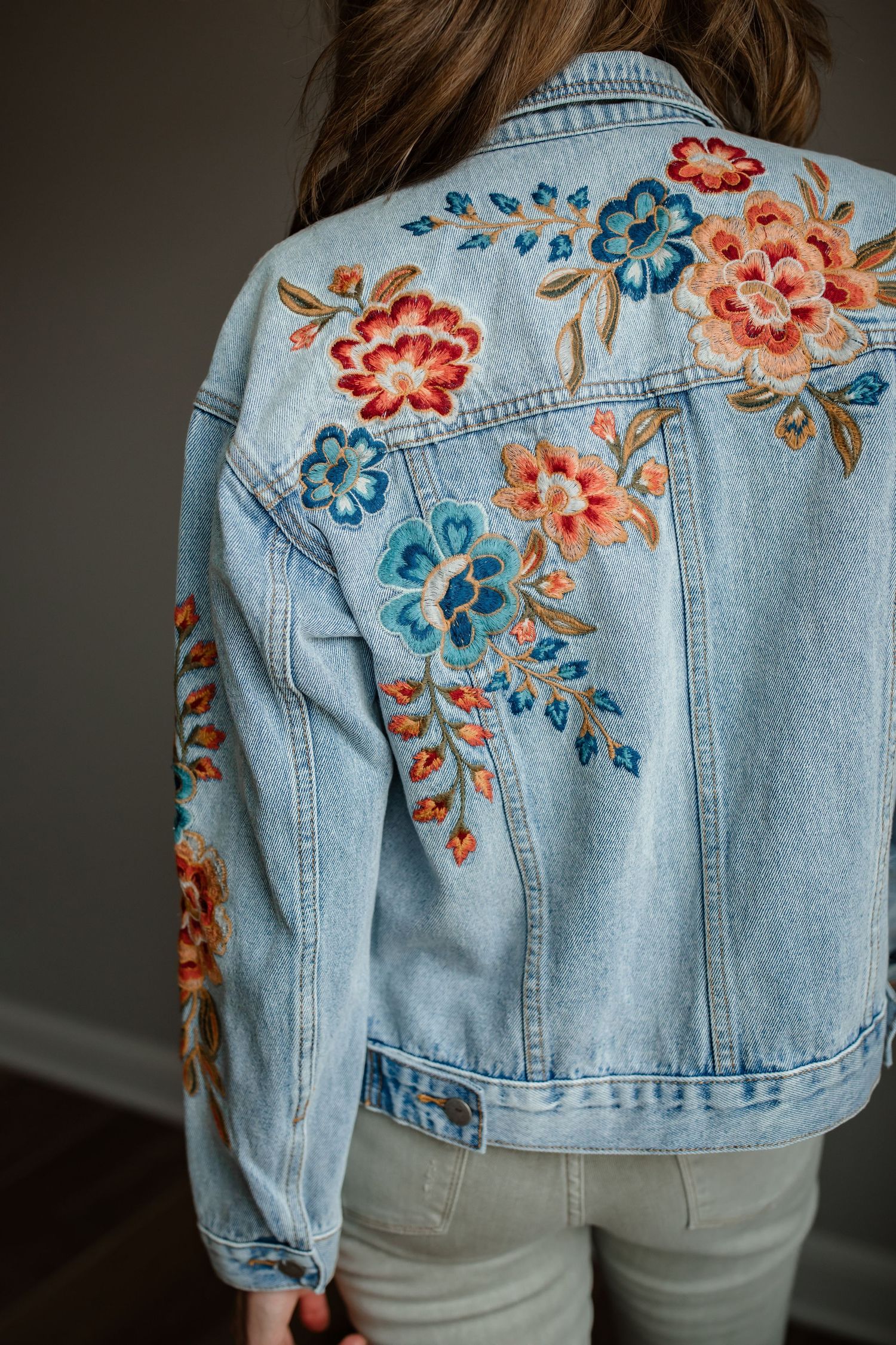 Light wash denim jacket with colorful floral embroidery featuring pink and blue blooms.