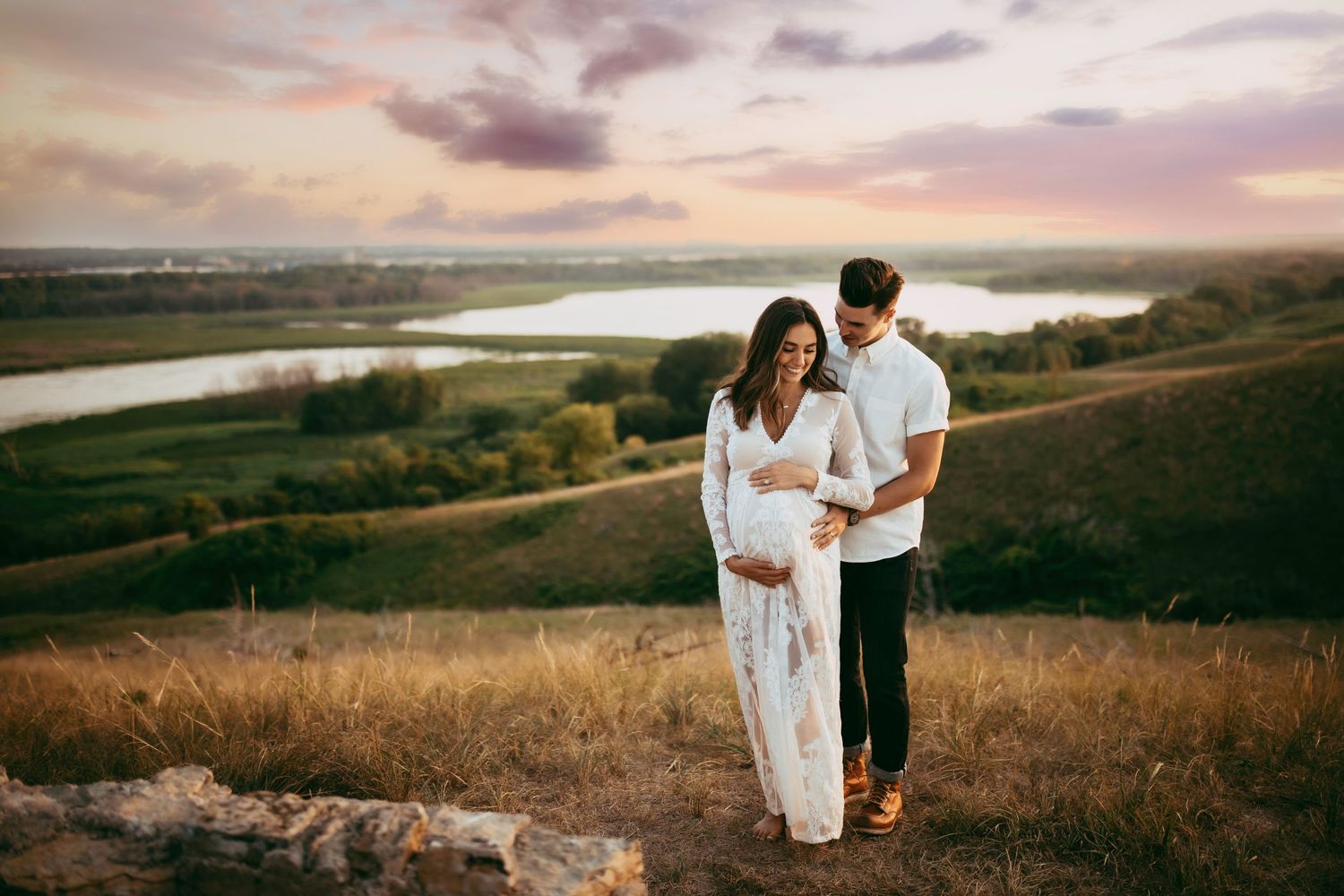 An intimate maternity photo session on a hilltop overlooking a winding river at dusk.