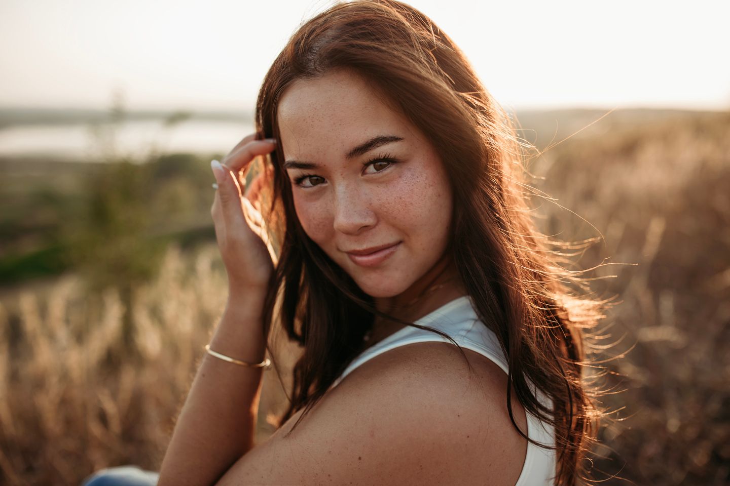 Portrait of woman with flowing dark hair in white top during golden hour.