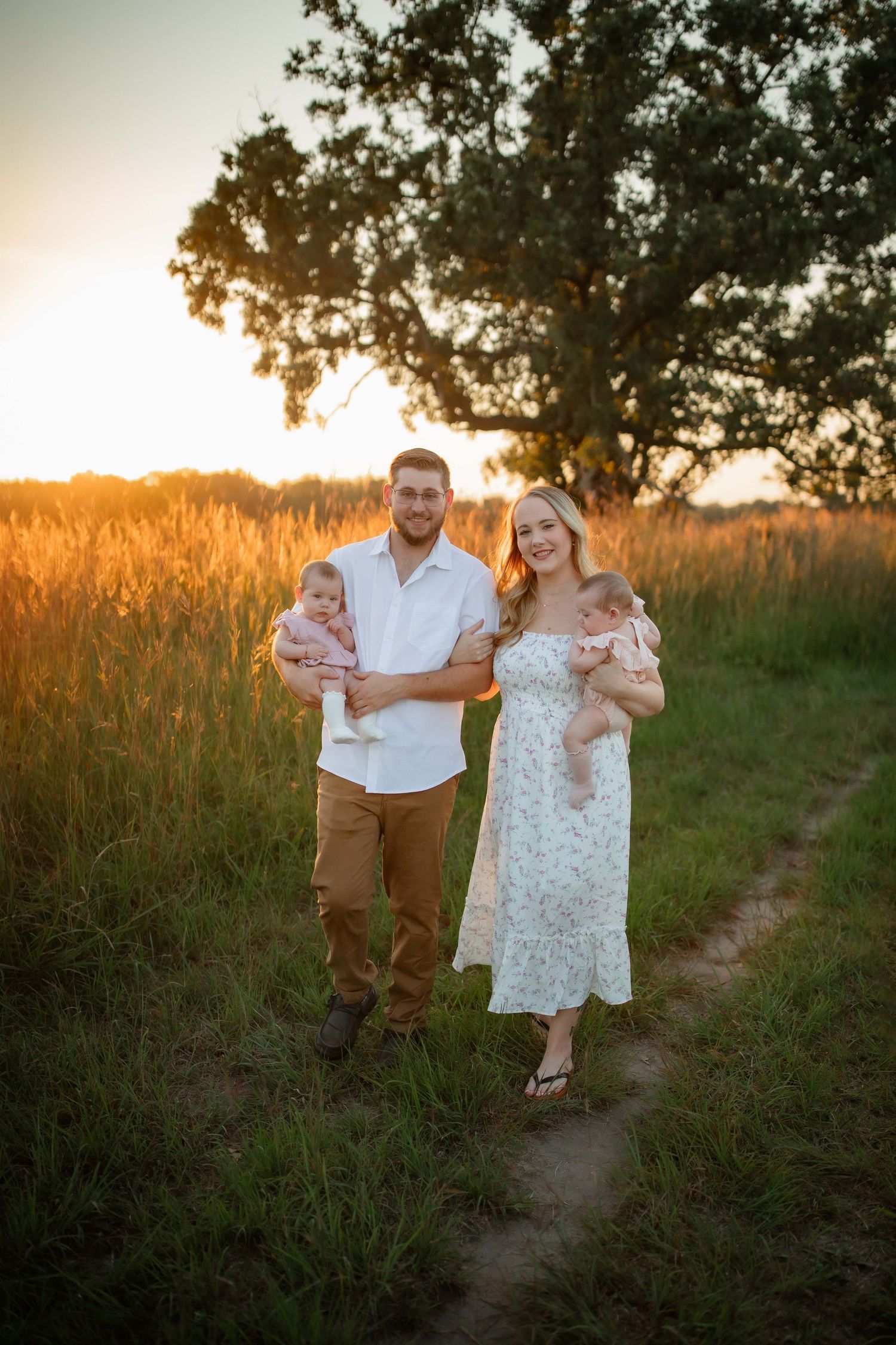 A family strolls along a dirt path through tall grass at sunset.