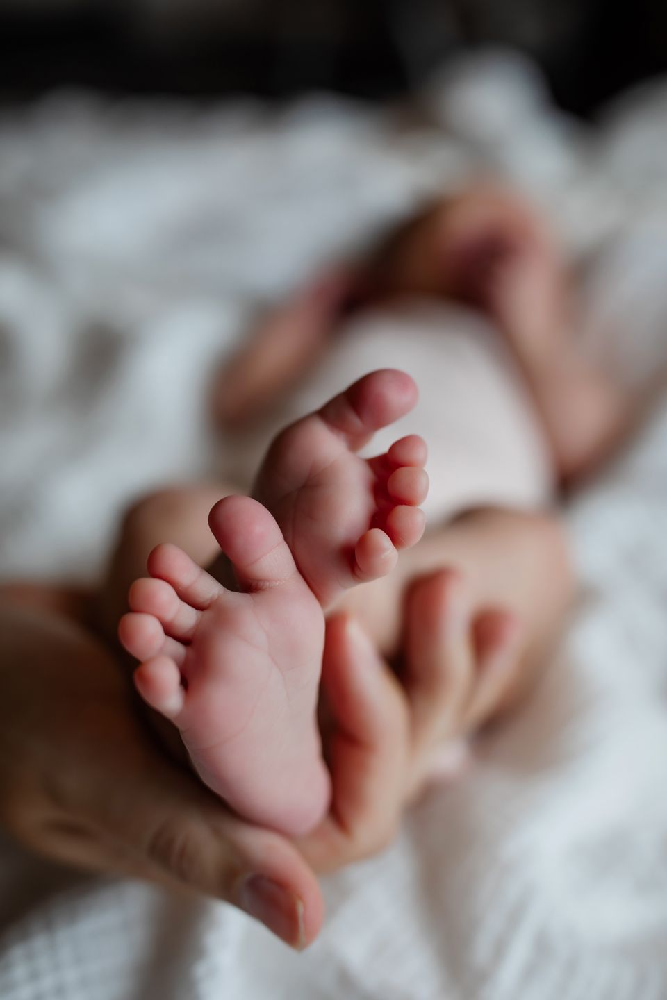 Close-up of tiny newborn feet and toes on white textured fabric.