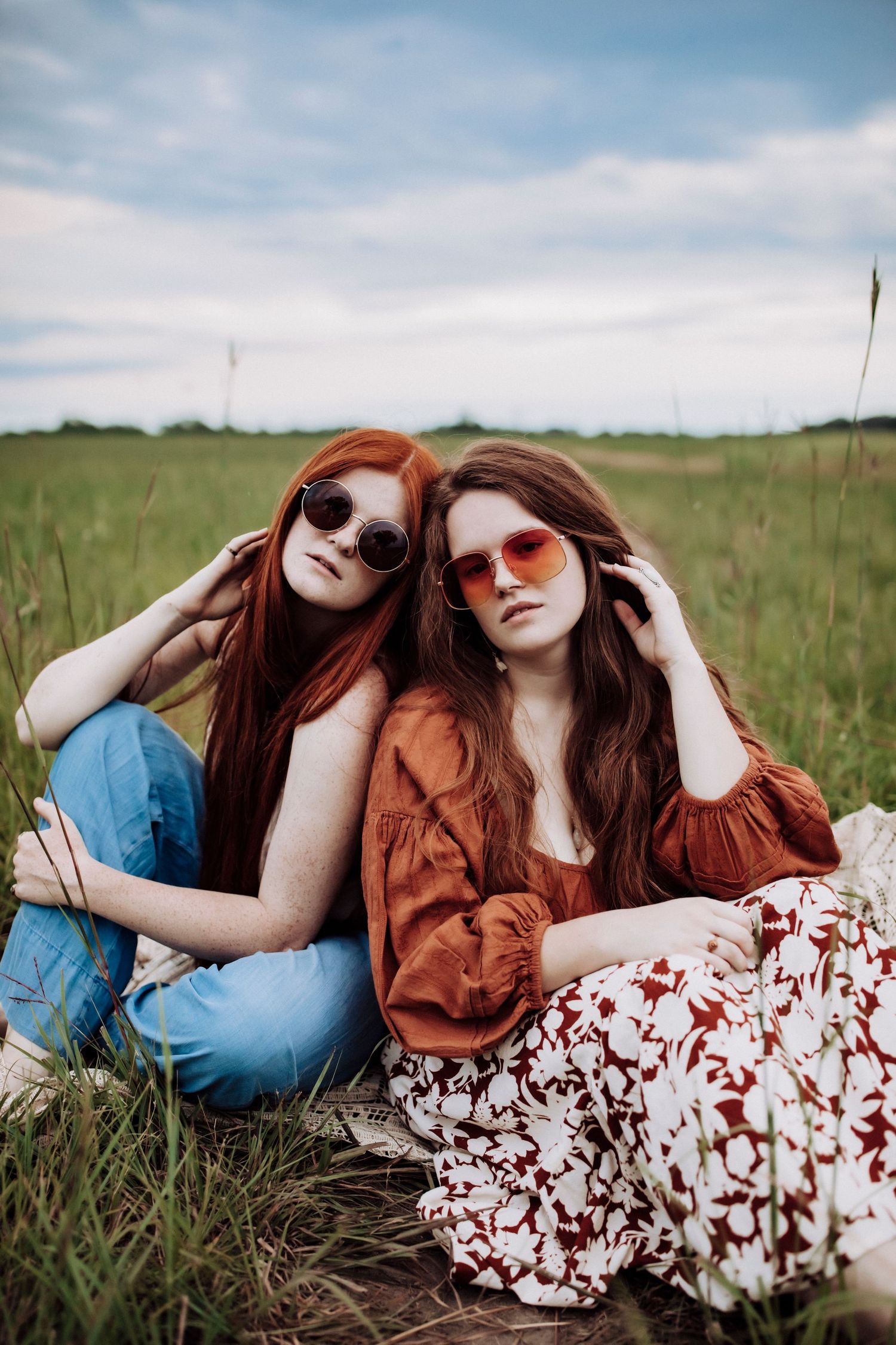Two friends in casual outfits and sunglasses relaxing in a sunny meadow.