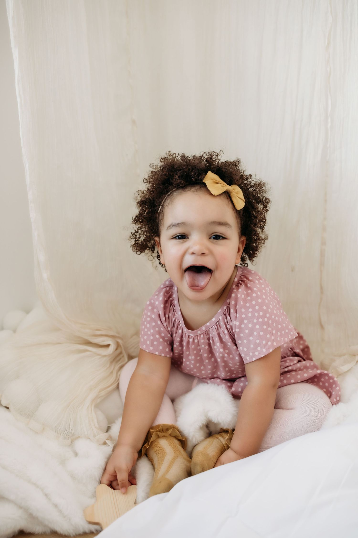 A smiling child in a pink dress plays on white bedding.