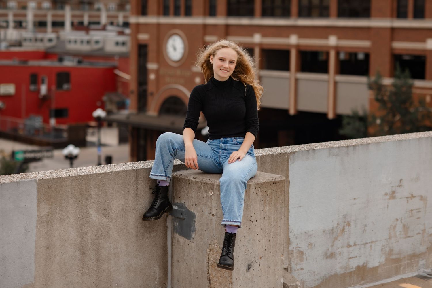 Casual urban portrait on a concrete ledge with light denim jeans and black sweater against city architecture.