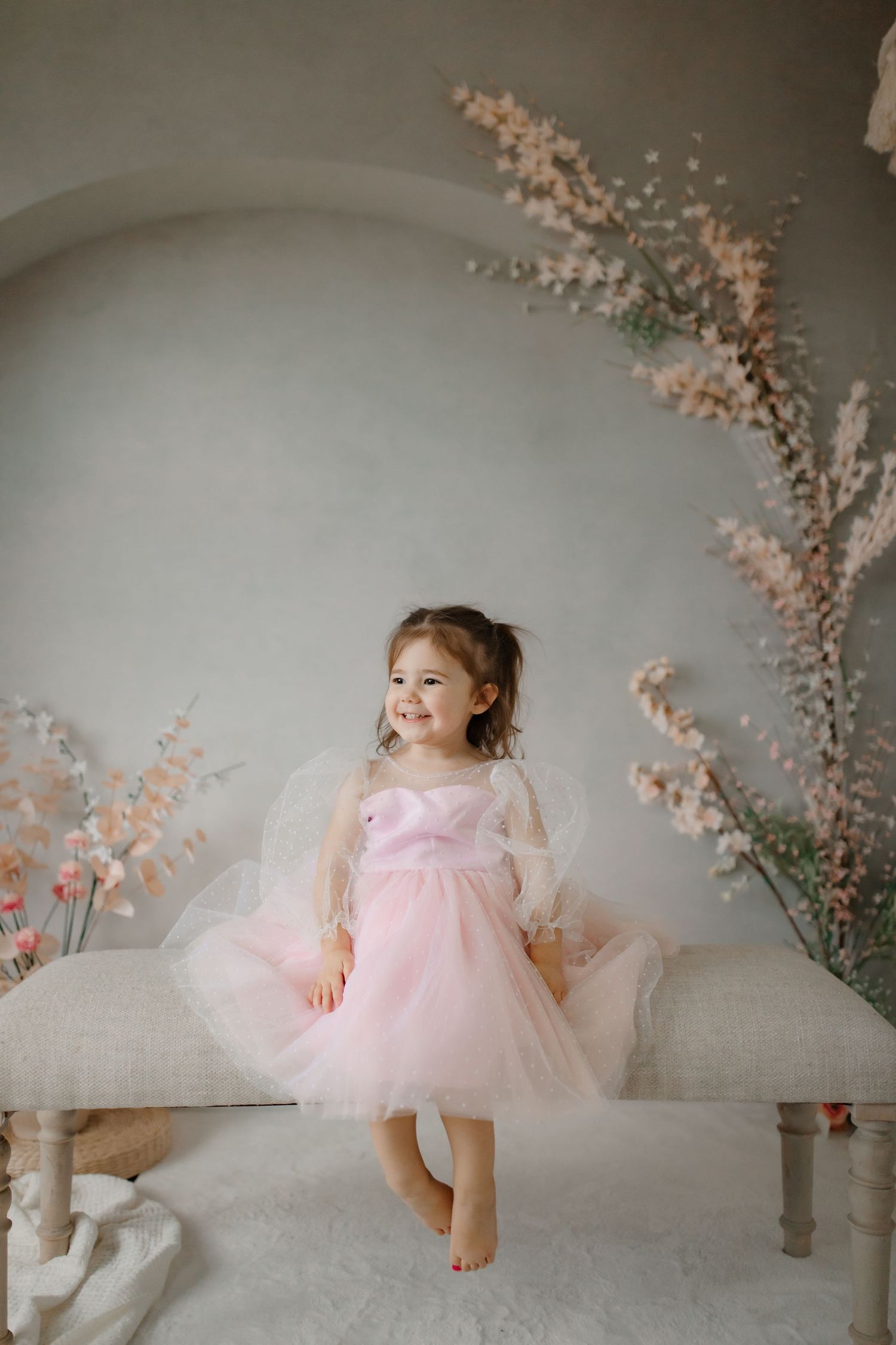 A joyful pose in a pink tulle dress on a white bench with floral decorations.