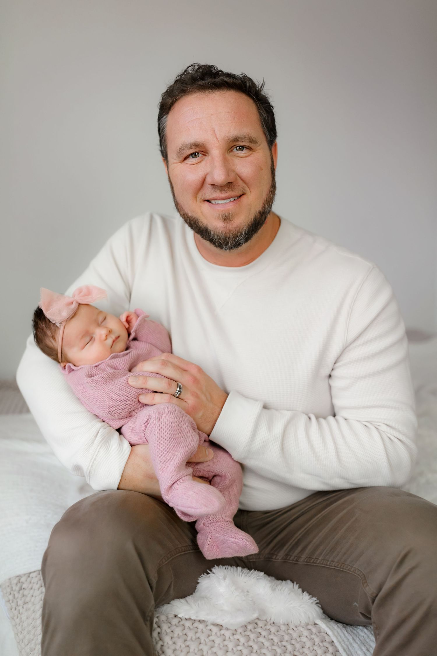 Adult in white sweater holding sleeping infant wearing pink outfit.