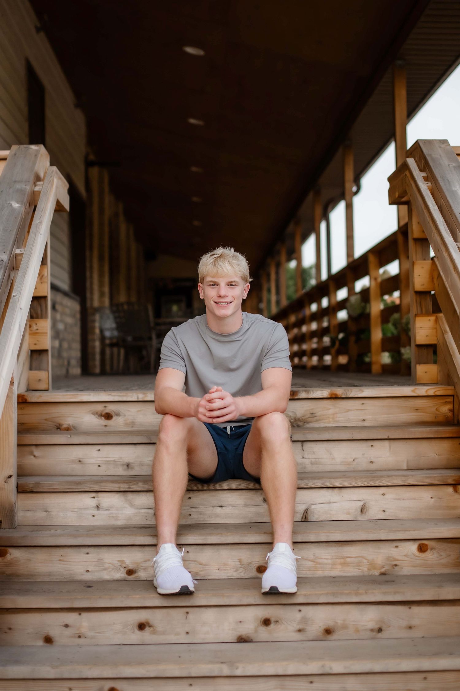 Casual portrait seated on wooden stairs with rustic architectural details.