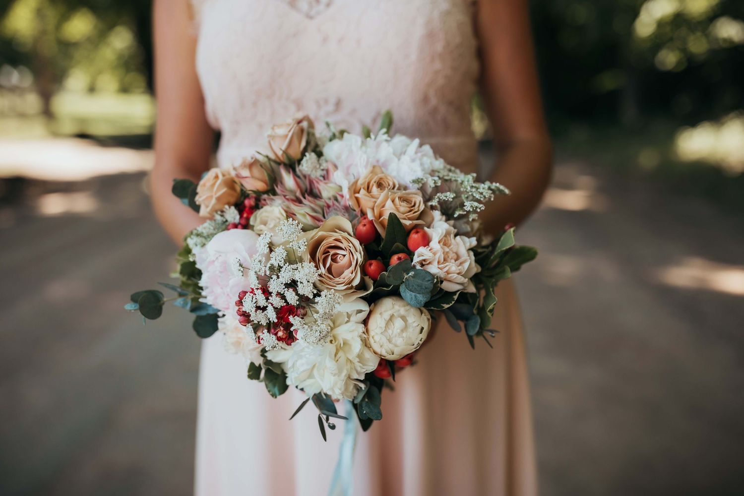 A delicate bridal bouquet featuring blush roses, white flowers, and greenery held against a light dress.