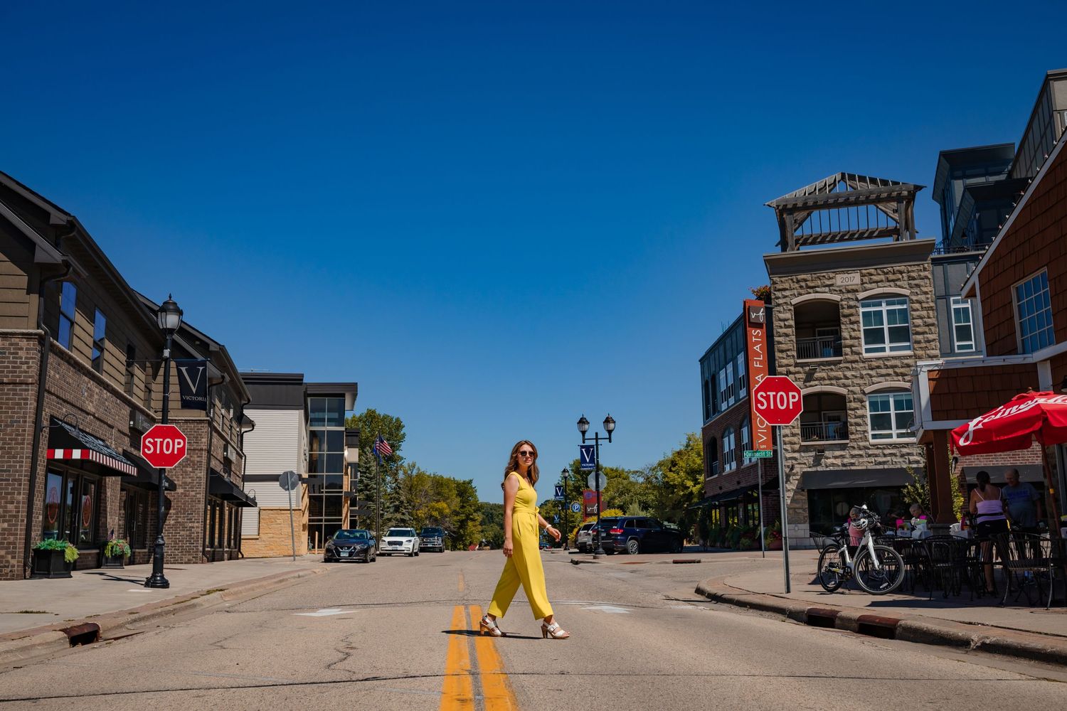 Woman in flowing yellow dress walks down center of small town main street on sunny day.