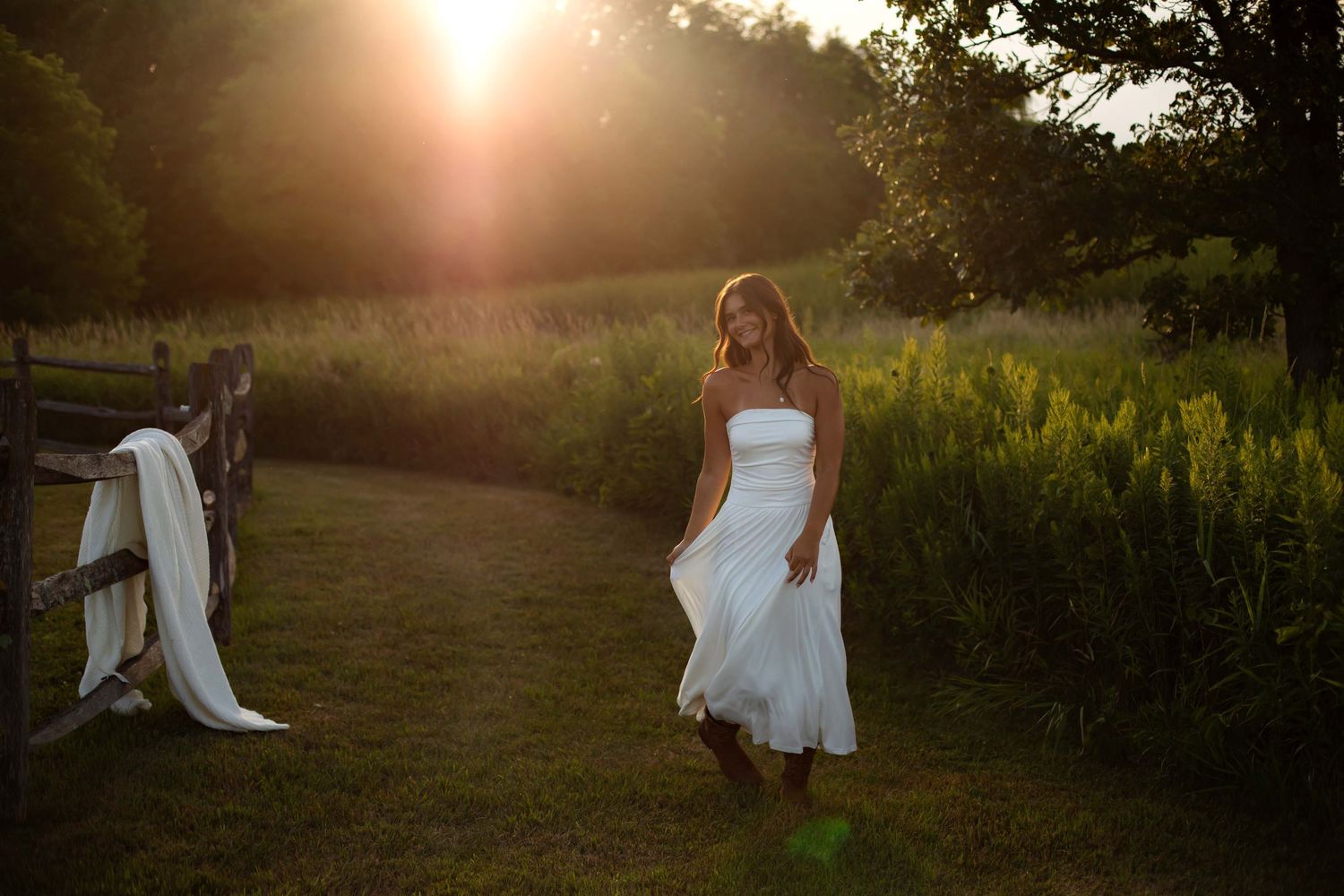 Woman in white dress walking on a sunlit garden path at golden hour.