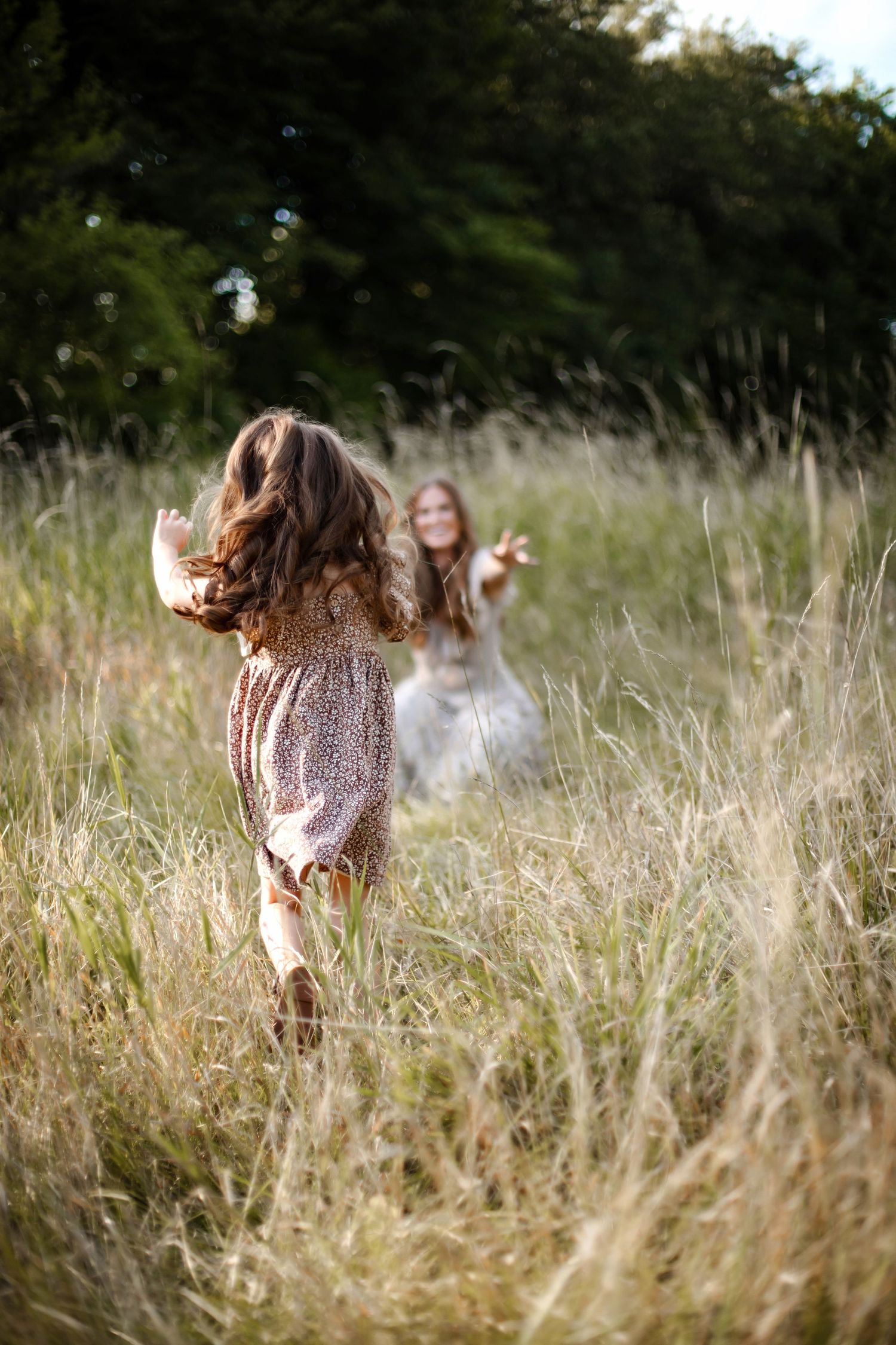 A dreamy summer scene shows people playing and running through tall golden grass in a sunlit meadow field.