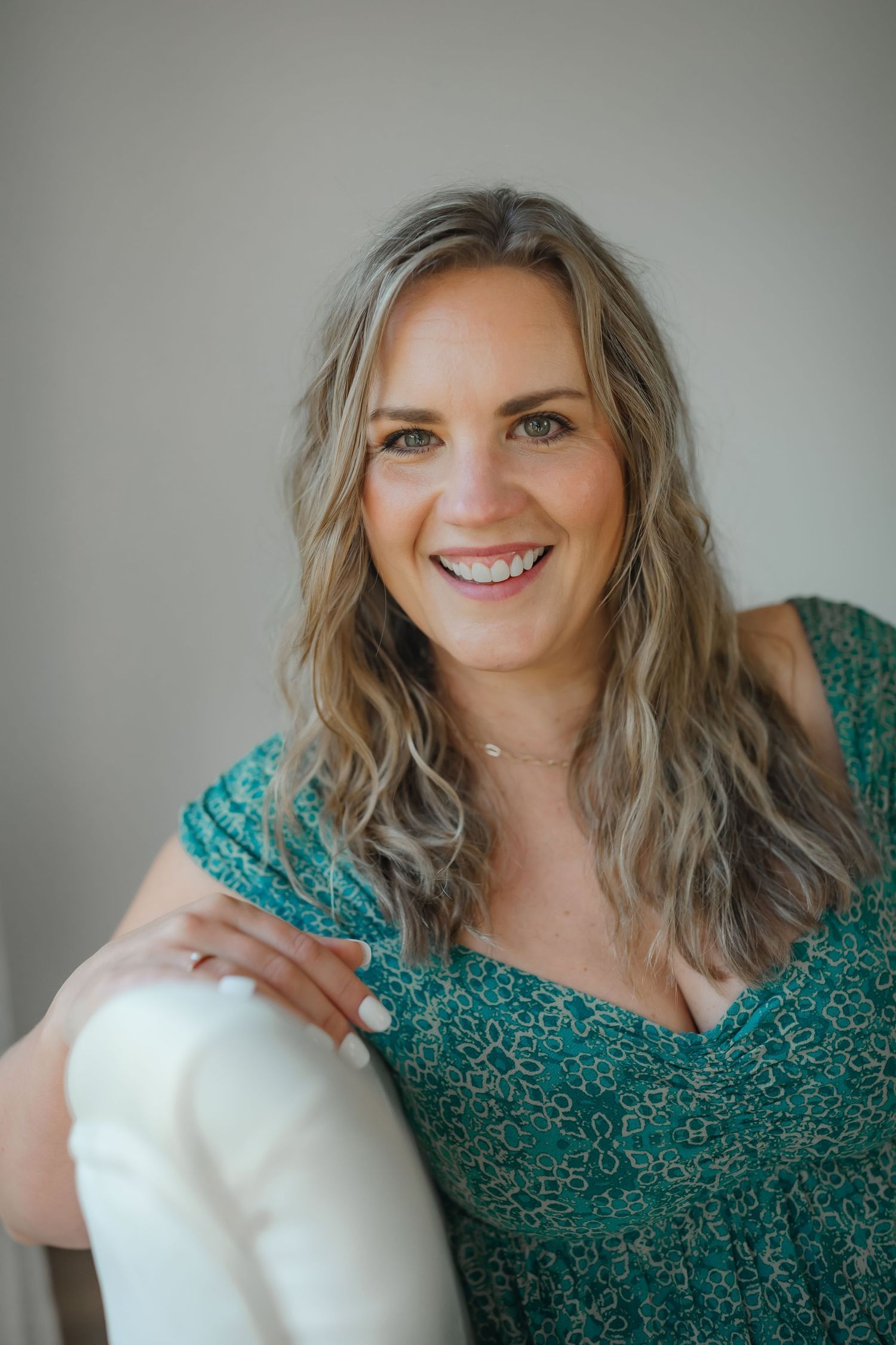 Casual portrait in teal patterned dress sitting on white furniture.