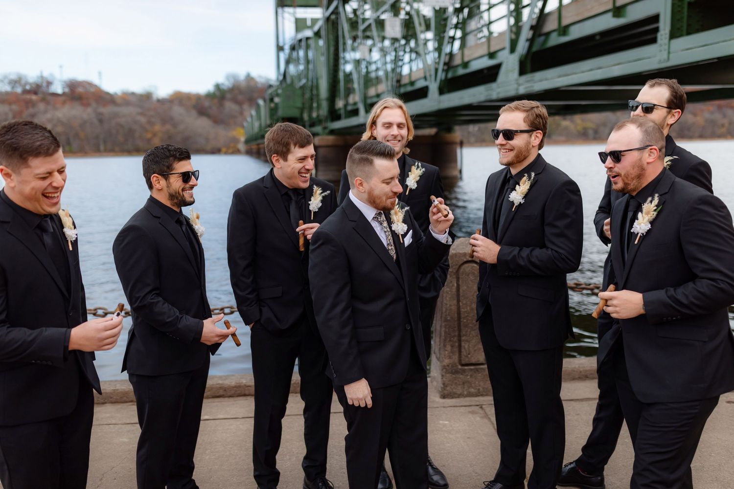Wedding party enjoys drinks and conversation by waterfront bridge.