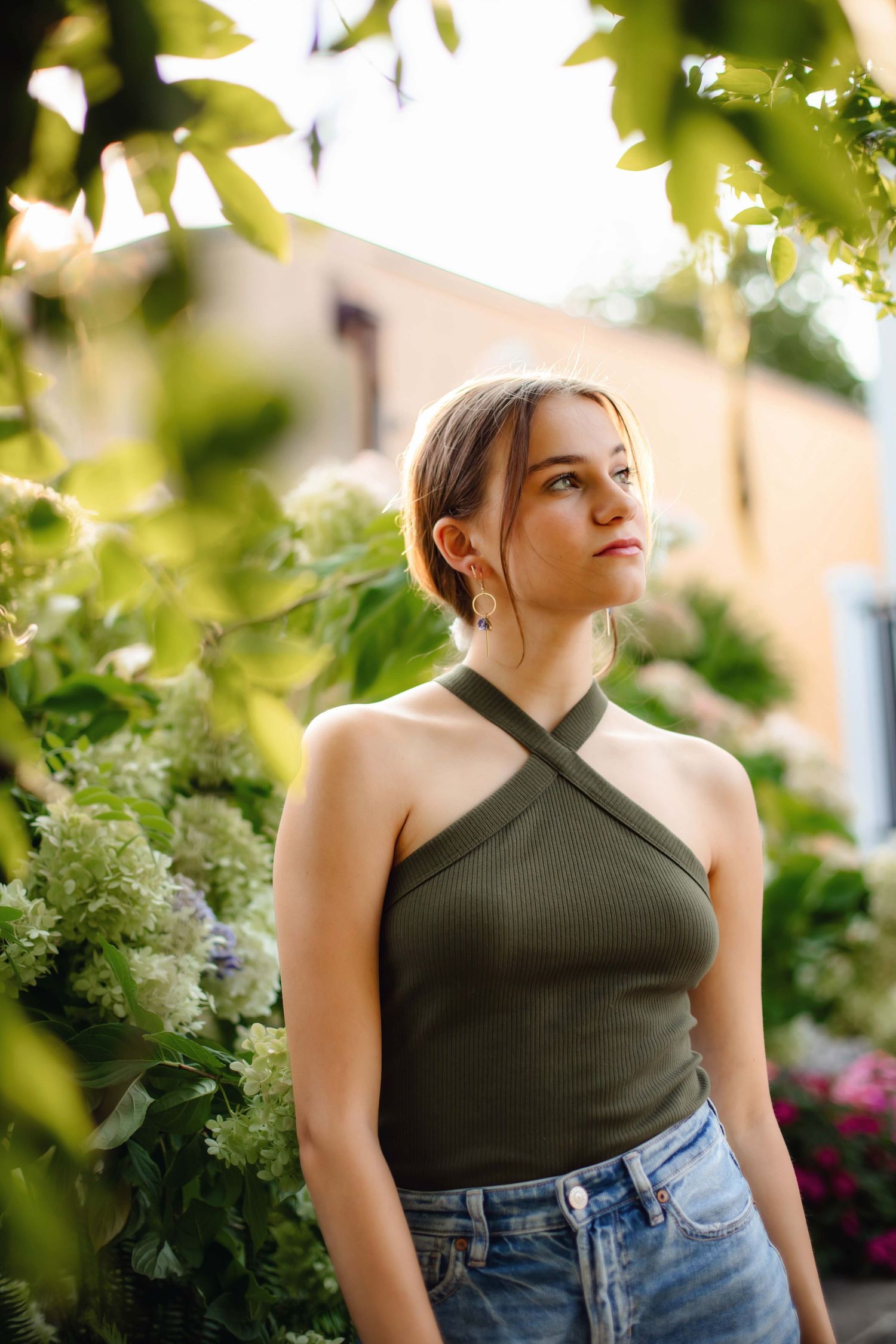 Person in halter top and jeans standing among blooming garden foliage.