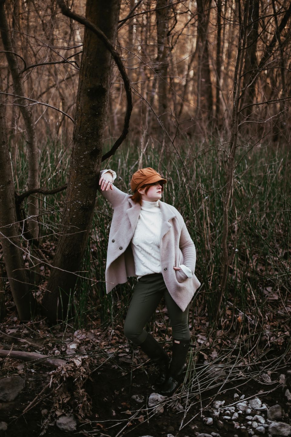 A dramatic pose among bare winter trees wearing a light coat and casual attire.