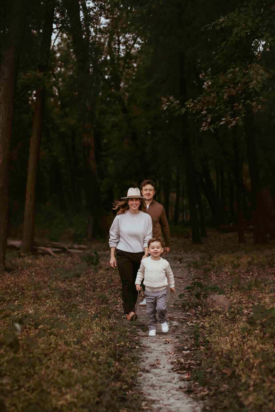 A family walks along a wooded trail in autumn.