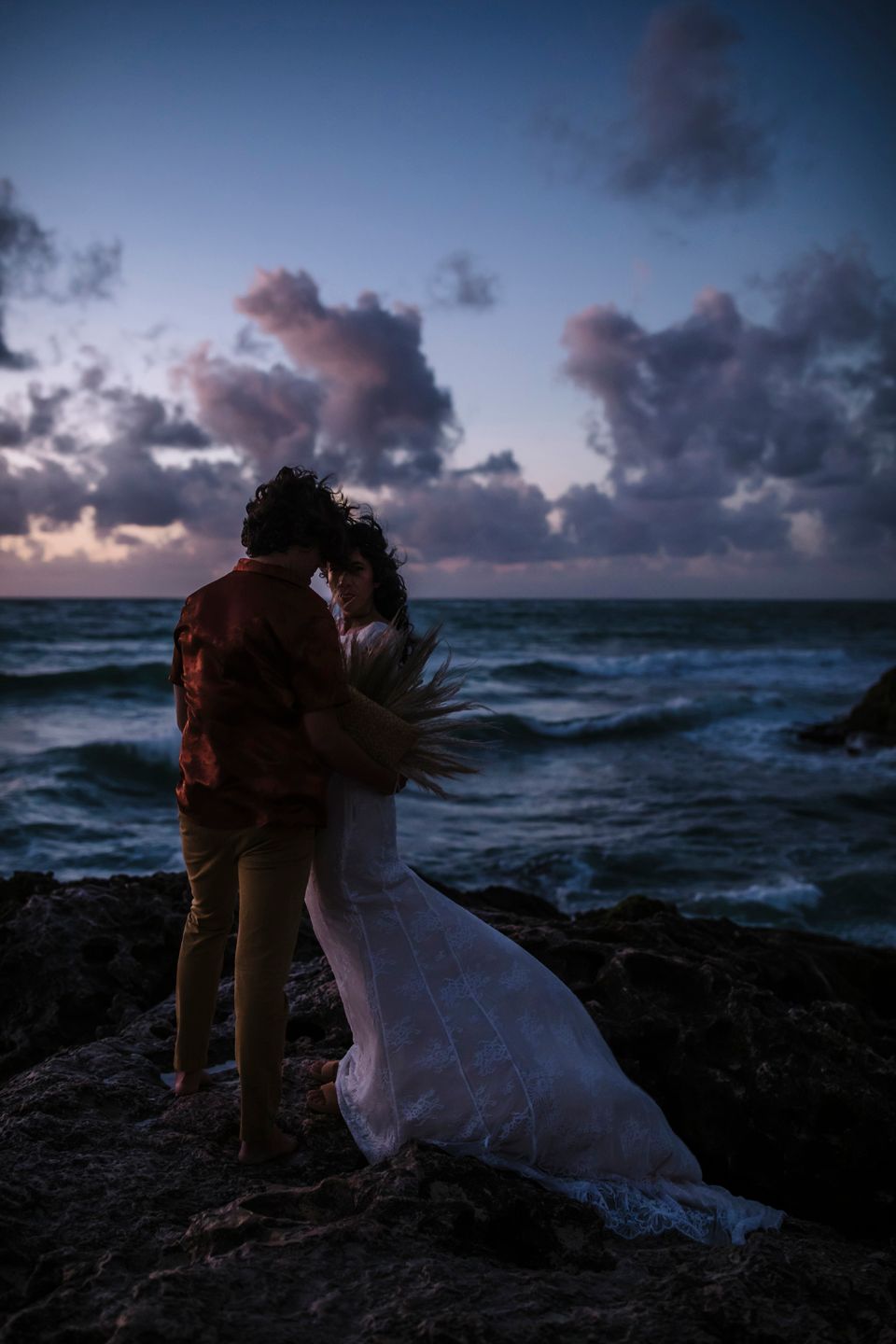 Dramatic oceanside wedding portrait at twilight with moody clouds and crashing waves.