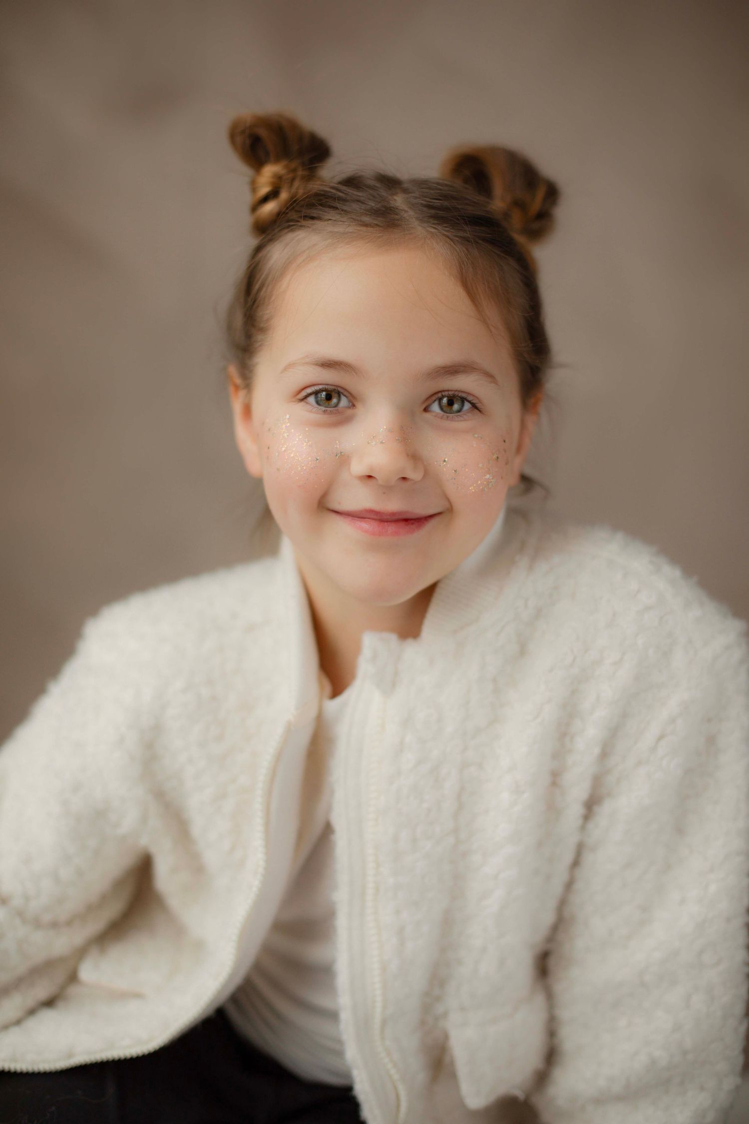 Portrait wearing a fluffy white cardigan with hair styled in two buns against a soft beige background.
