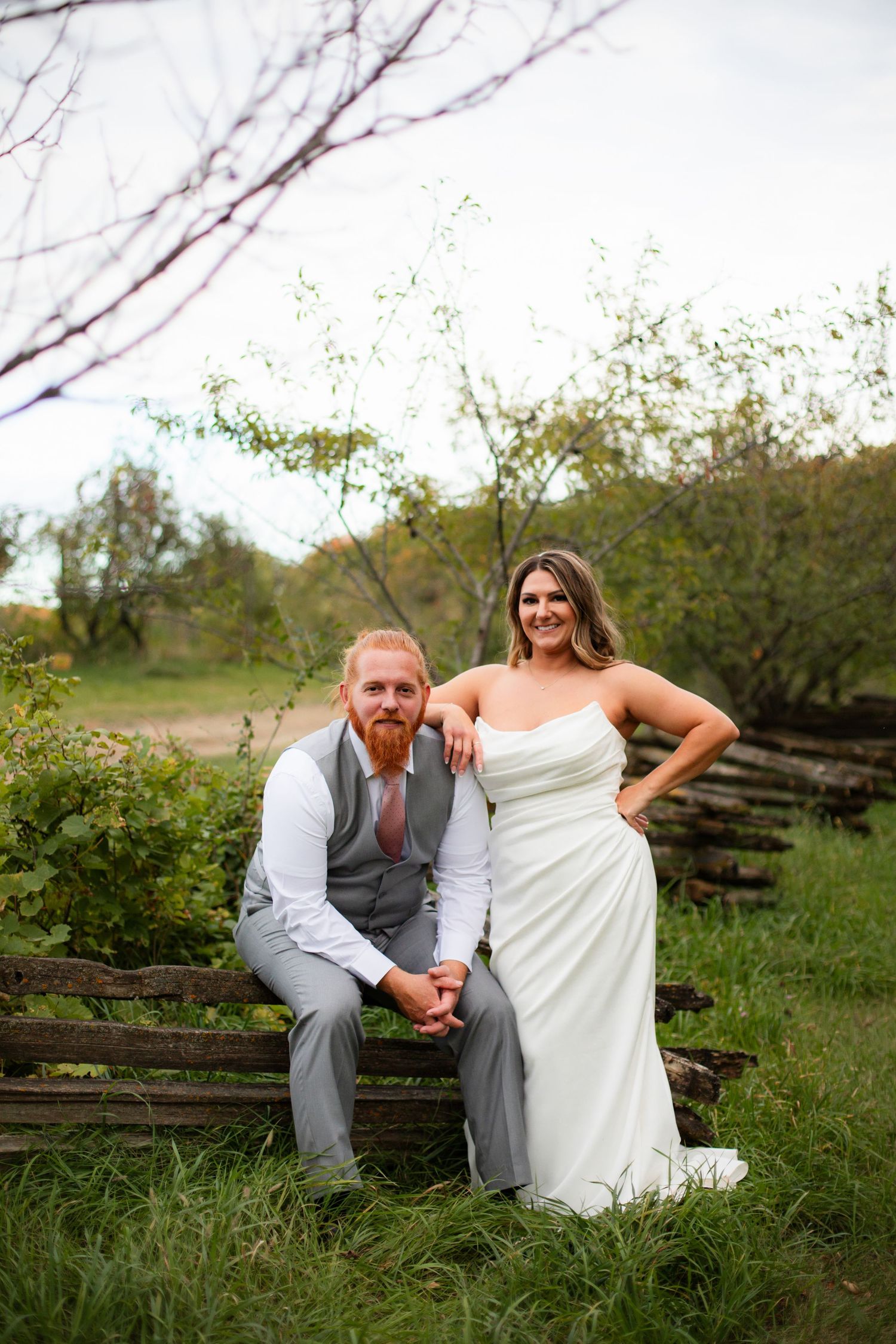 A couple in wedding attire poses casually on wooden steps in a natural outdoor setting.