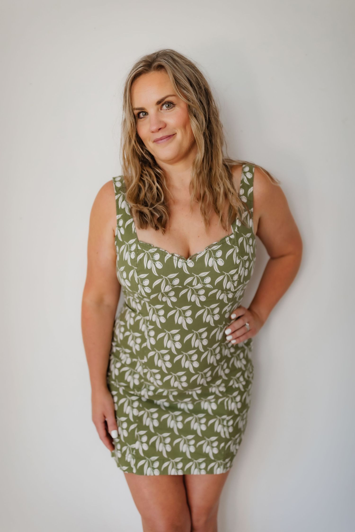 Summer fashion portrait in olive green floral mini dress against white wall.