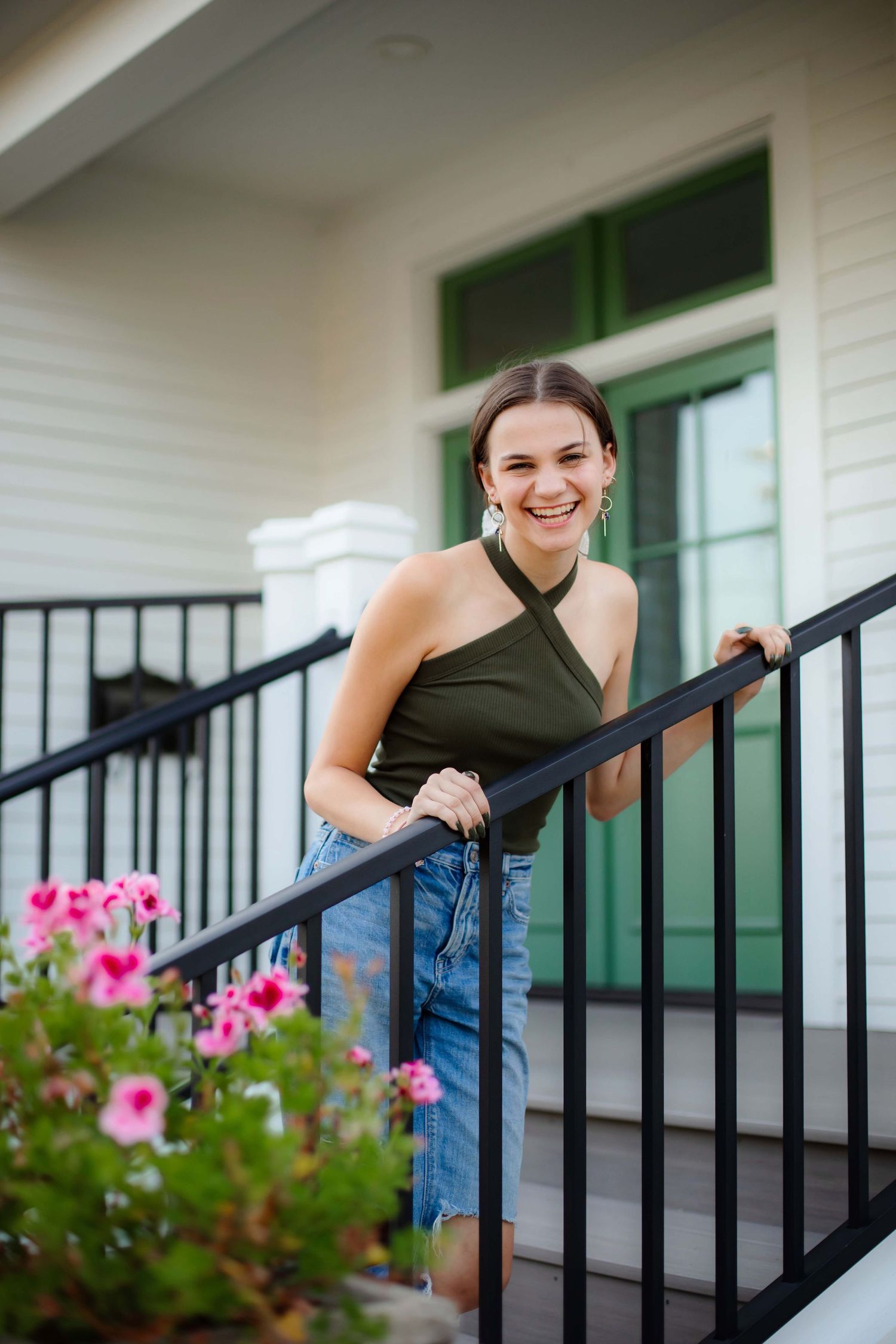 Person in casual attire smiling on white porch with pink flowers blooming nearby.