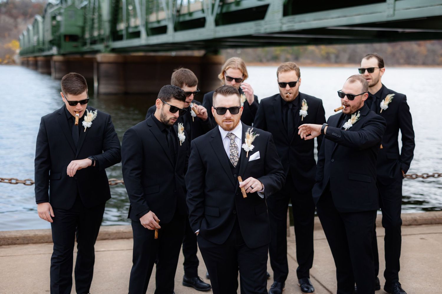 Wedding party in dark suits checking their watches in coordinated pose by bridge.