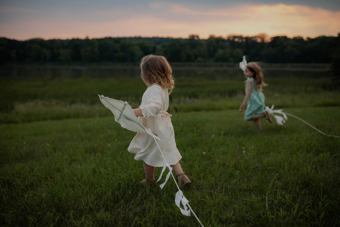 Two people in white dresses play in a grassy field at sunset.
