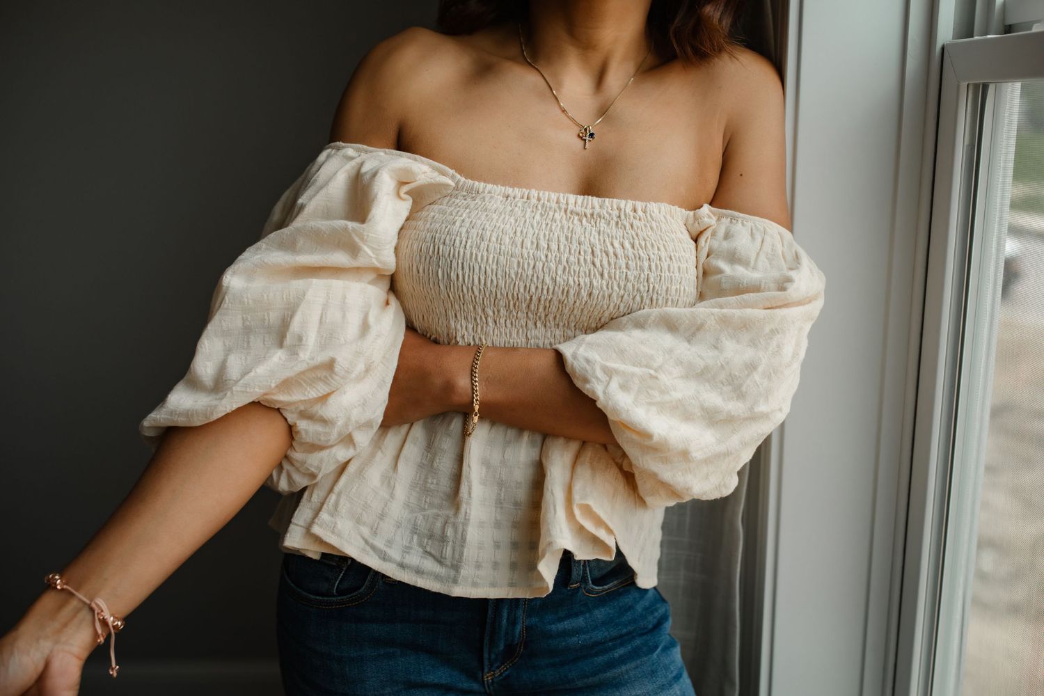Off-shoulder cream smocked crop top with puff sleeves styled with blue jeans for a casual summer look.