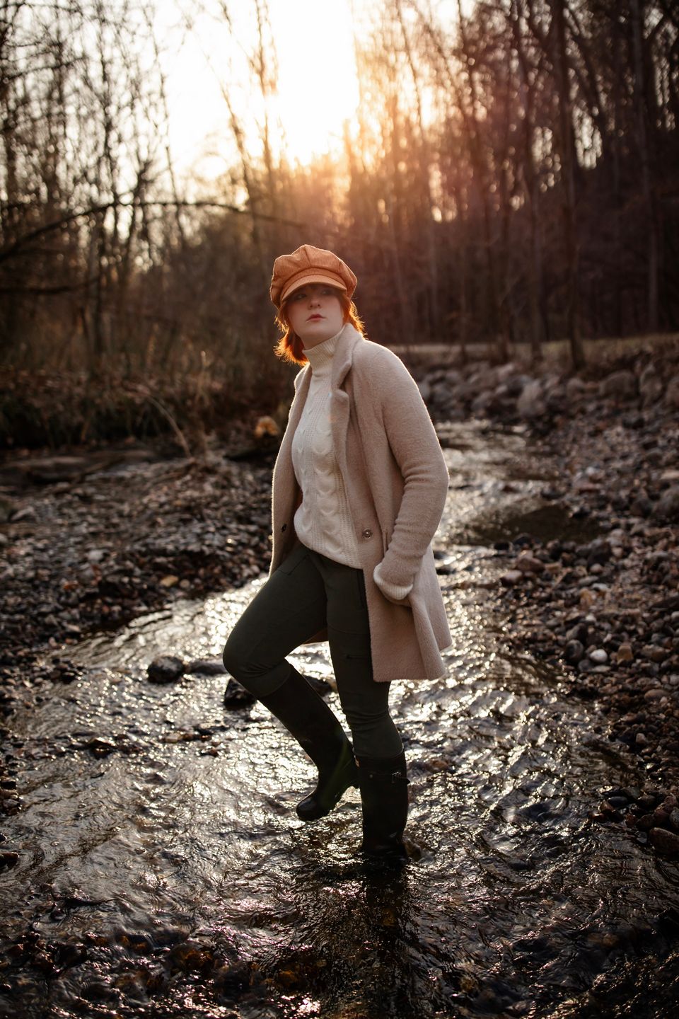 A winter scene at sunset with boots splashing in a stream while wearing a beige coat.