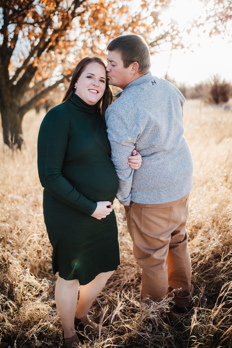 A tender autumn portrait of a sweet couple embracing in a field with golden grass and autumn trees in the background.