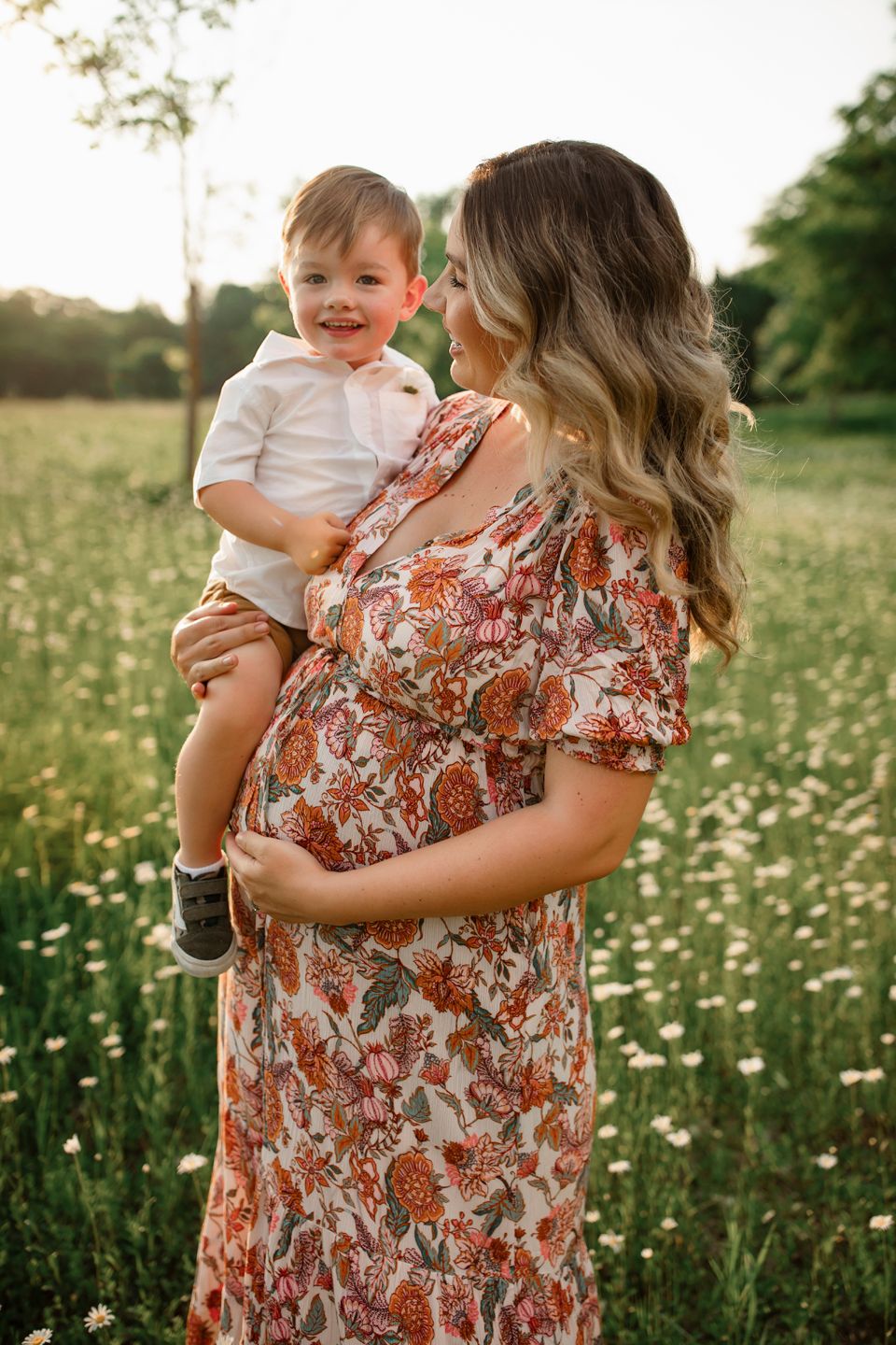 Parent and child share a tender moment in a wildflower meadow at sunset wearing floral dress and white outfit.