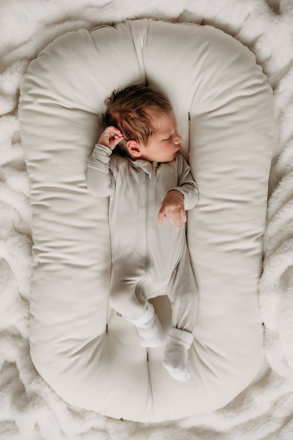 Sleeping baby in gray onesie on white lounger pillow.